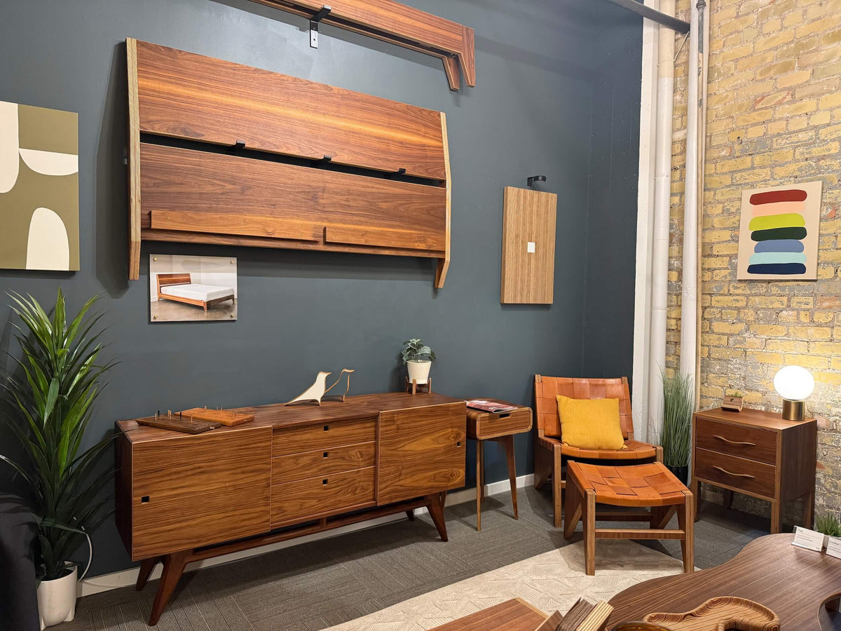 Wooden furniture including a headboard, sideboard, and chairs in a room with gray walls and brick accents.
