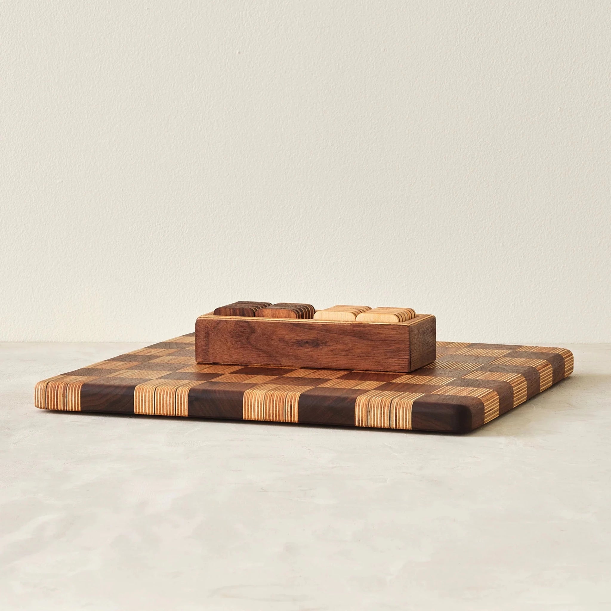Striped checkerboard board topped with walnut tray of stacked checkers pieces, front view