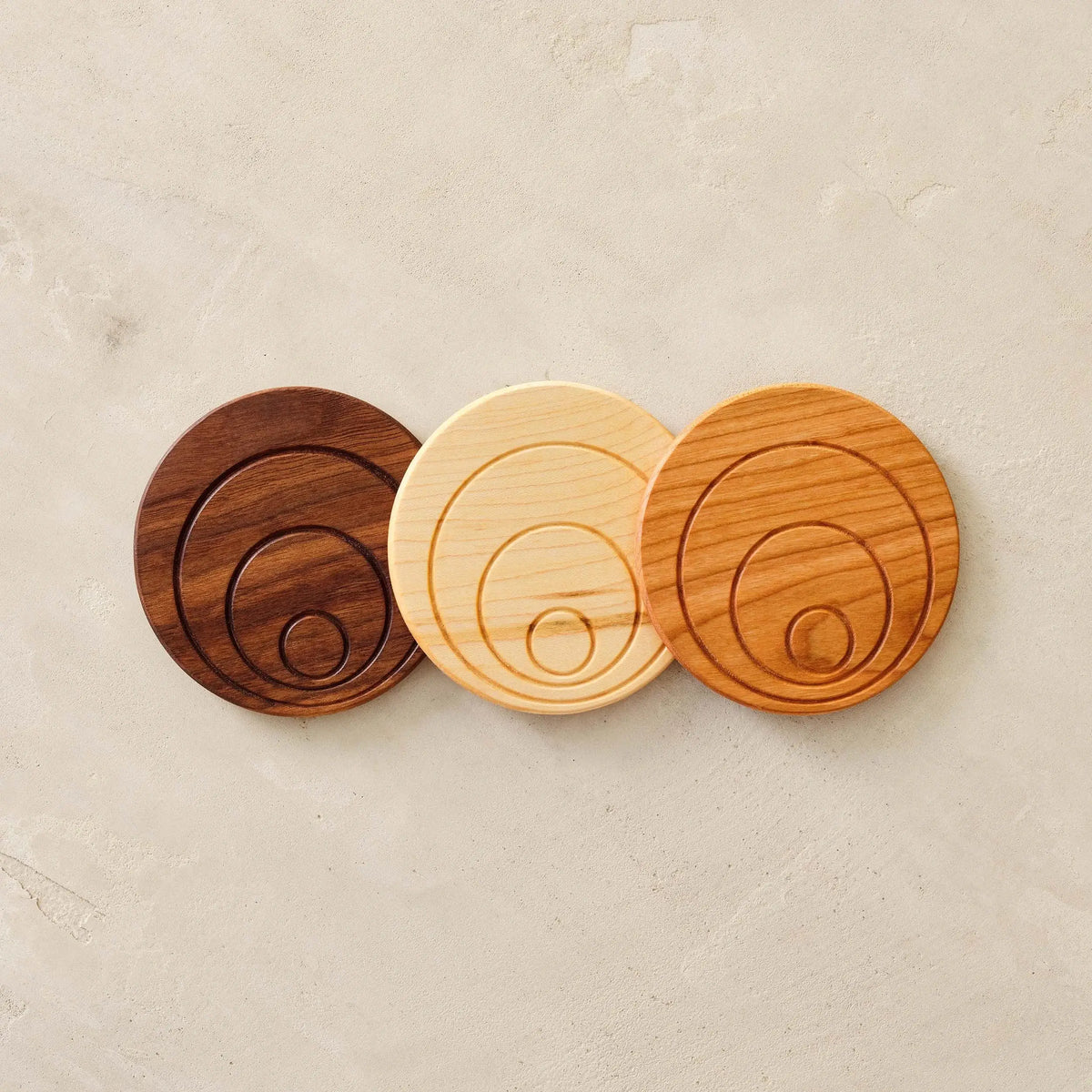 Three coasters side by side—walnut, maple, cherry—showing concentric circle grooves