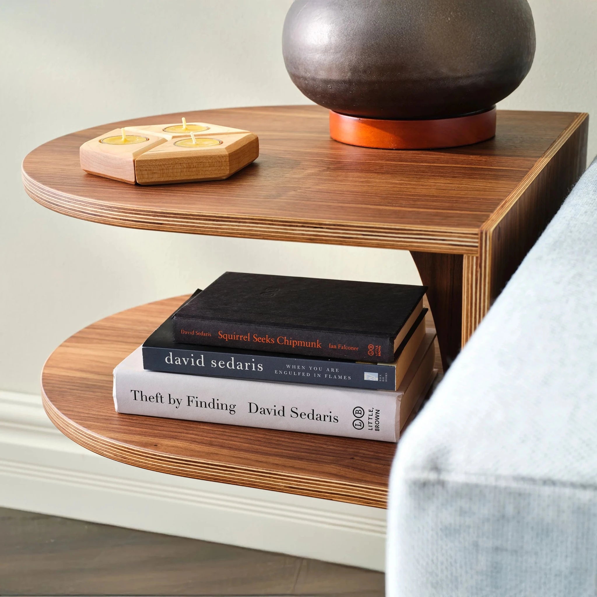 Walnut End Table No. 2 lower shelf with books, candle holder, gray sofa beside