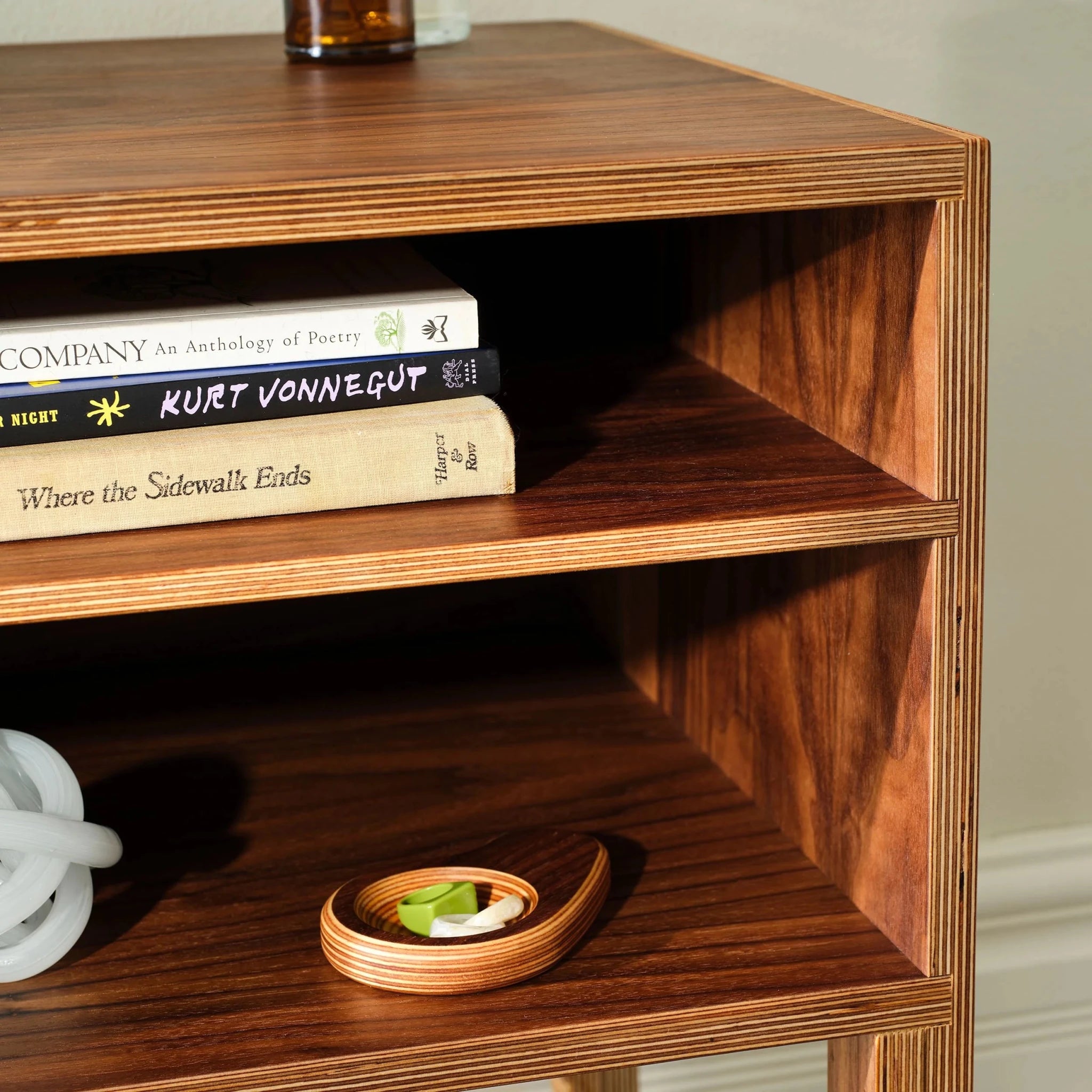 Close-up of walnut nightstand shelf with book spines and birch catchall tray