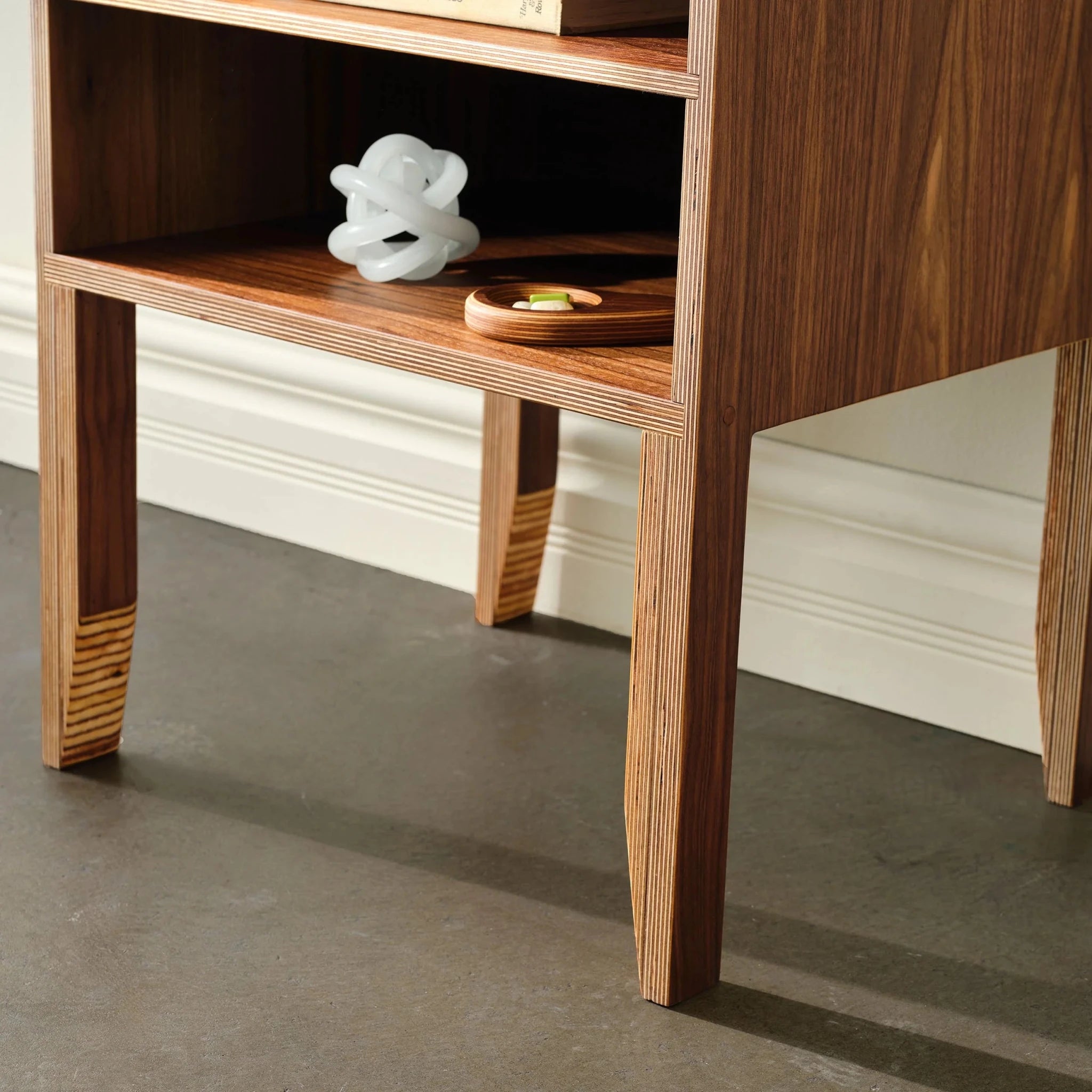 Close-up of walnut nightstand legs and shelf with white knot sculpture, tray