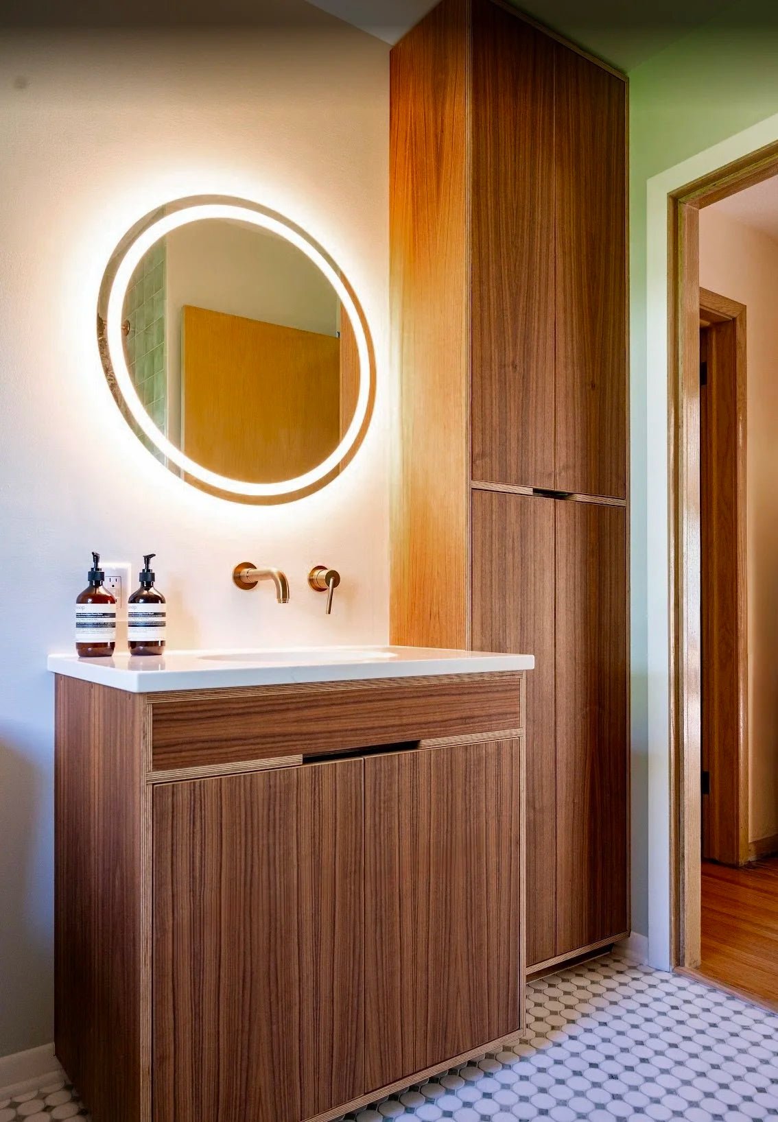 Floating walnut vanity with tall linen tower, round LED mirror, mosaic tile floor