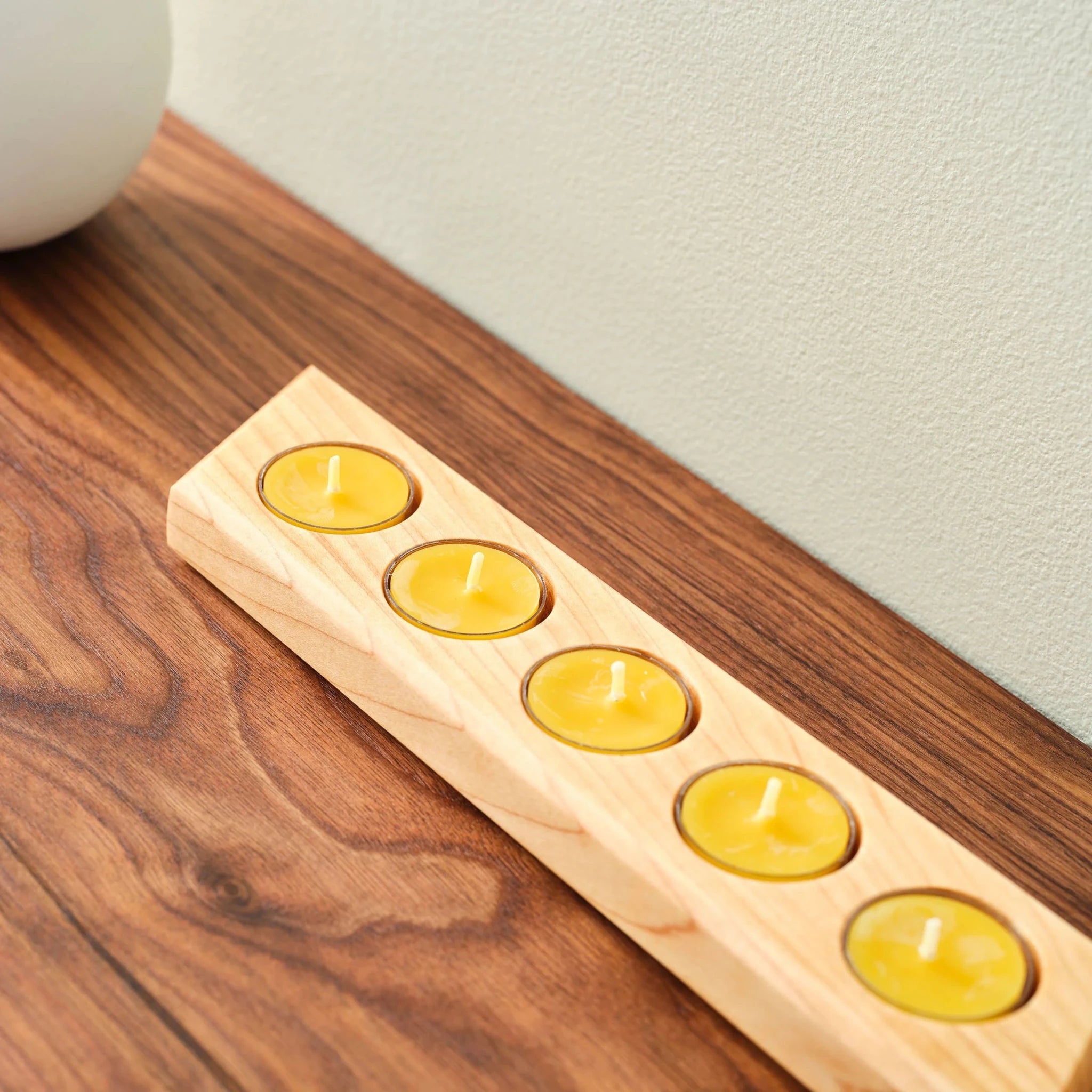 Maple tealight bar with five yellow candles on walnut table beside white vase