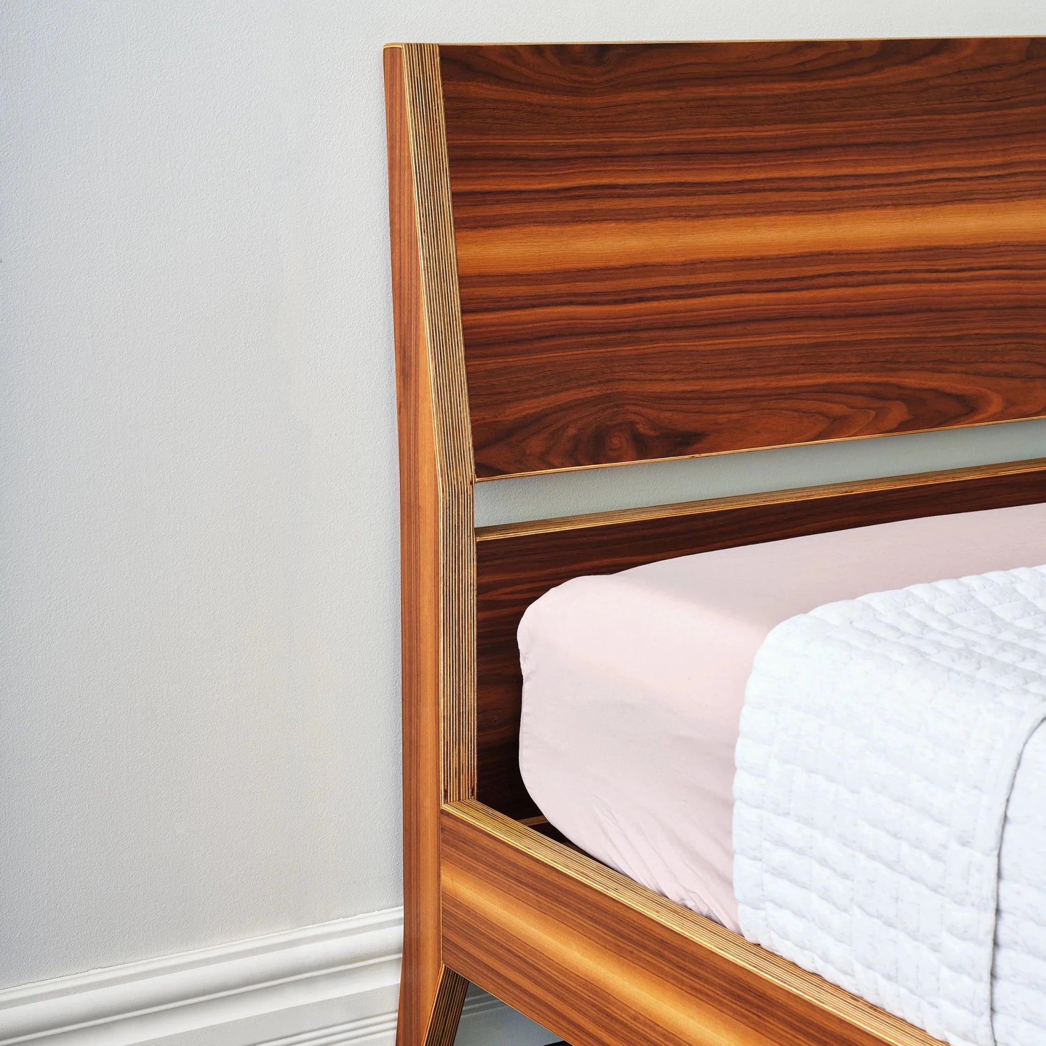 Walnut platform bed headboard and angled leg from foot view, pink bedding