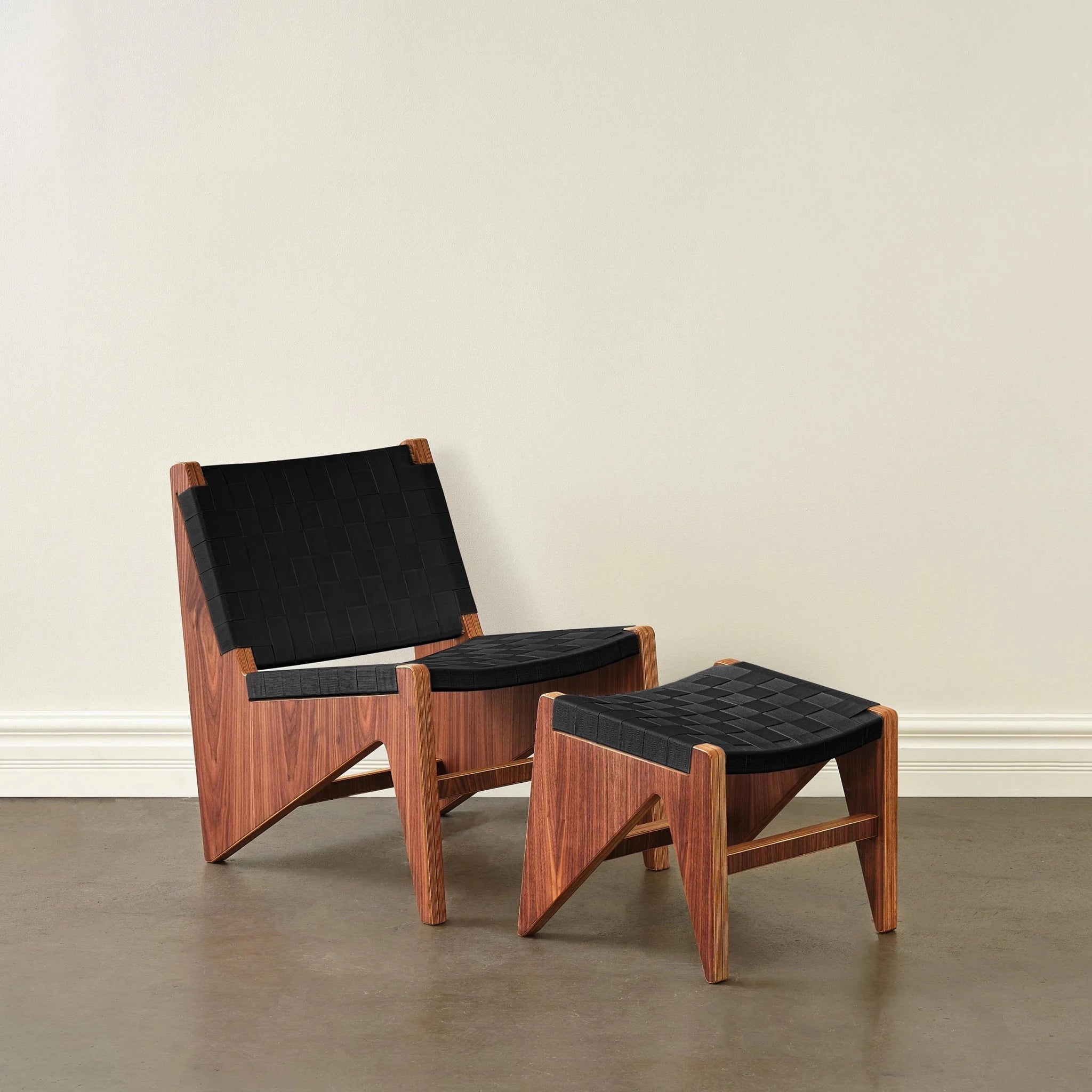 Walnut accent chair and ottoman with woven black fabric straps, front view, neutral wall