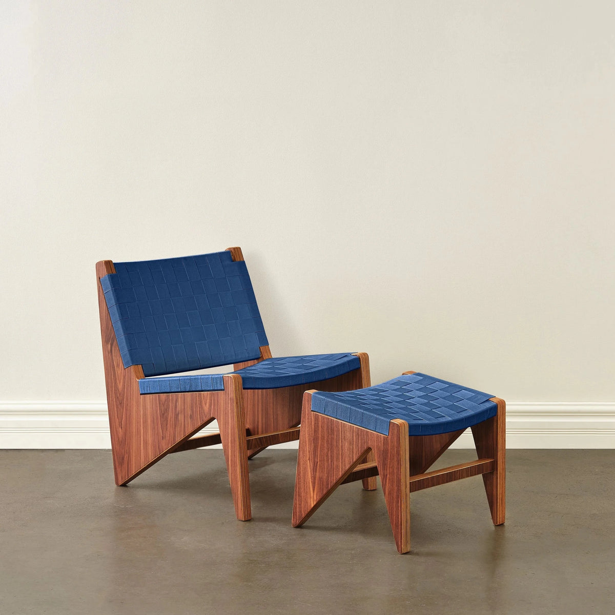 Walnut accent chair and ottoman with woven navy-blue fabric straps, front angle, concrete floor