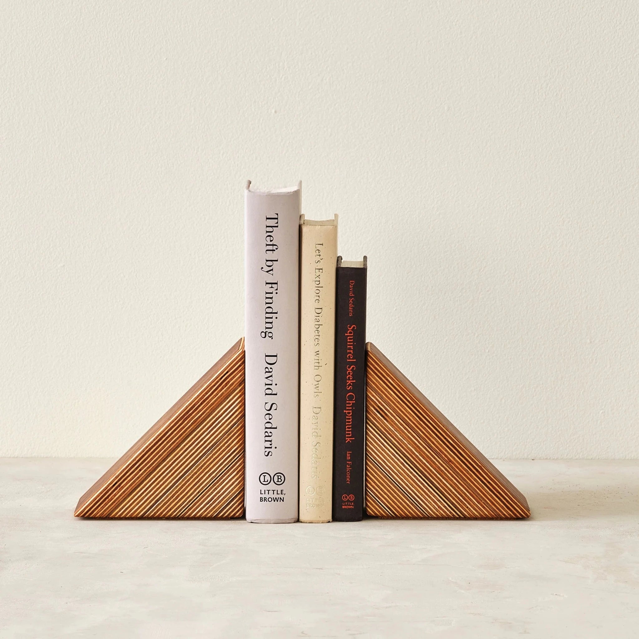 Wide triangular layered-birch bookends bracketing three upright books, striped grain facing forward