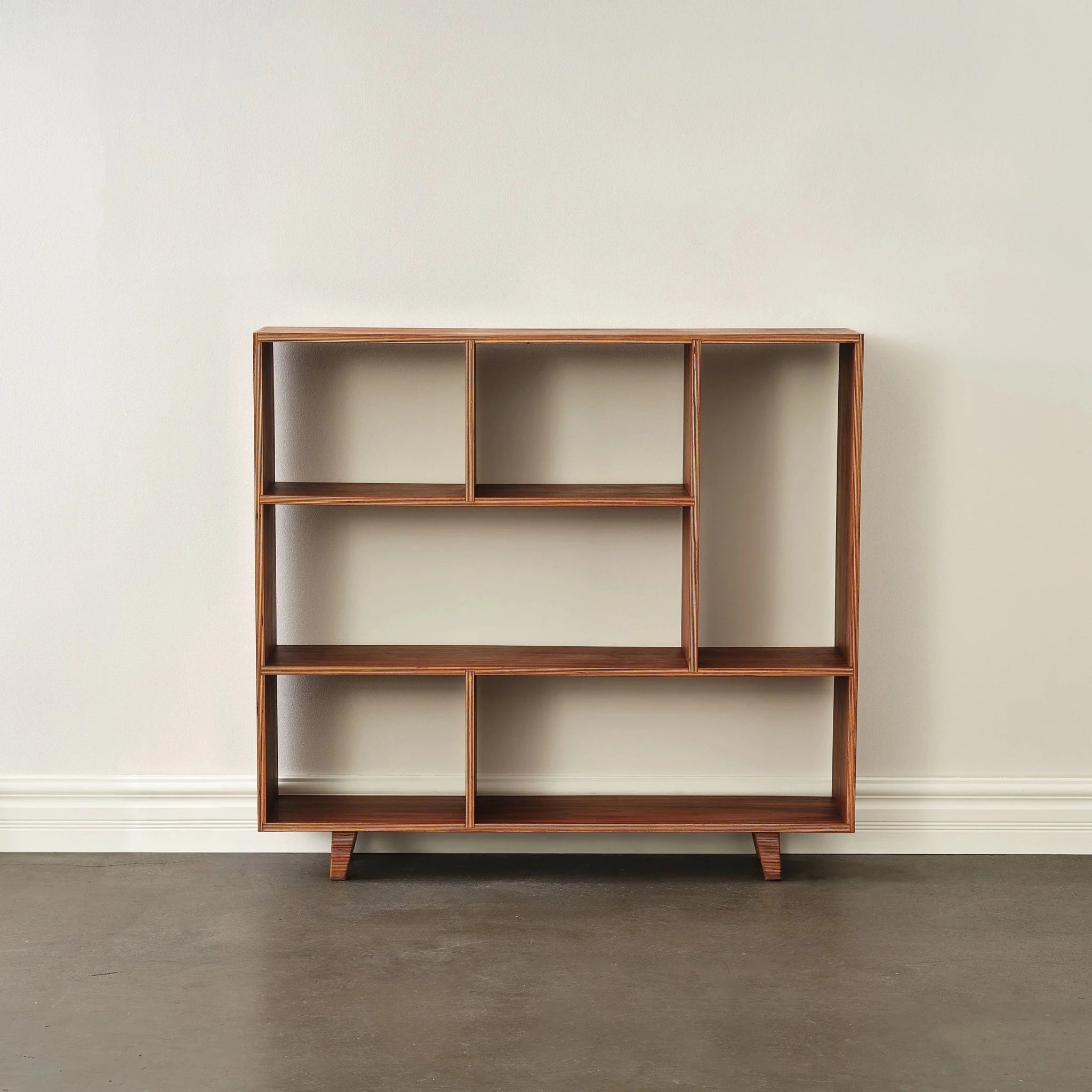 Empty walnut bookcase with asymmetric shelves, front view against white wall