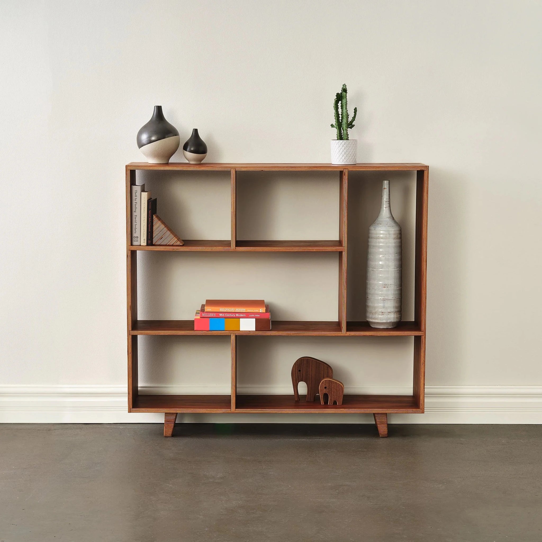Staged walnut bookcase with ceramic vases, cactus, books, and wooden elephants