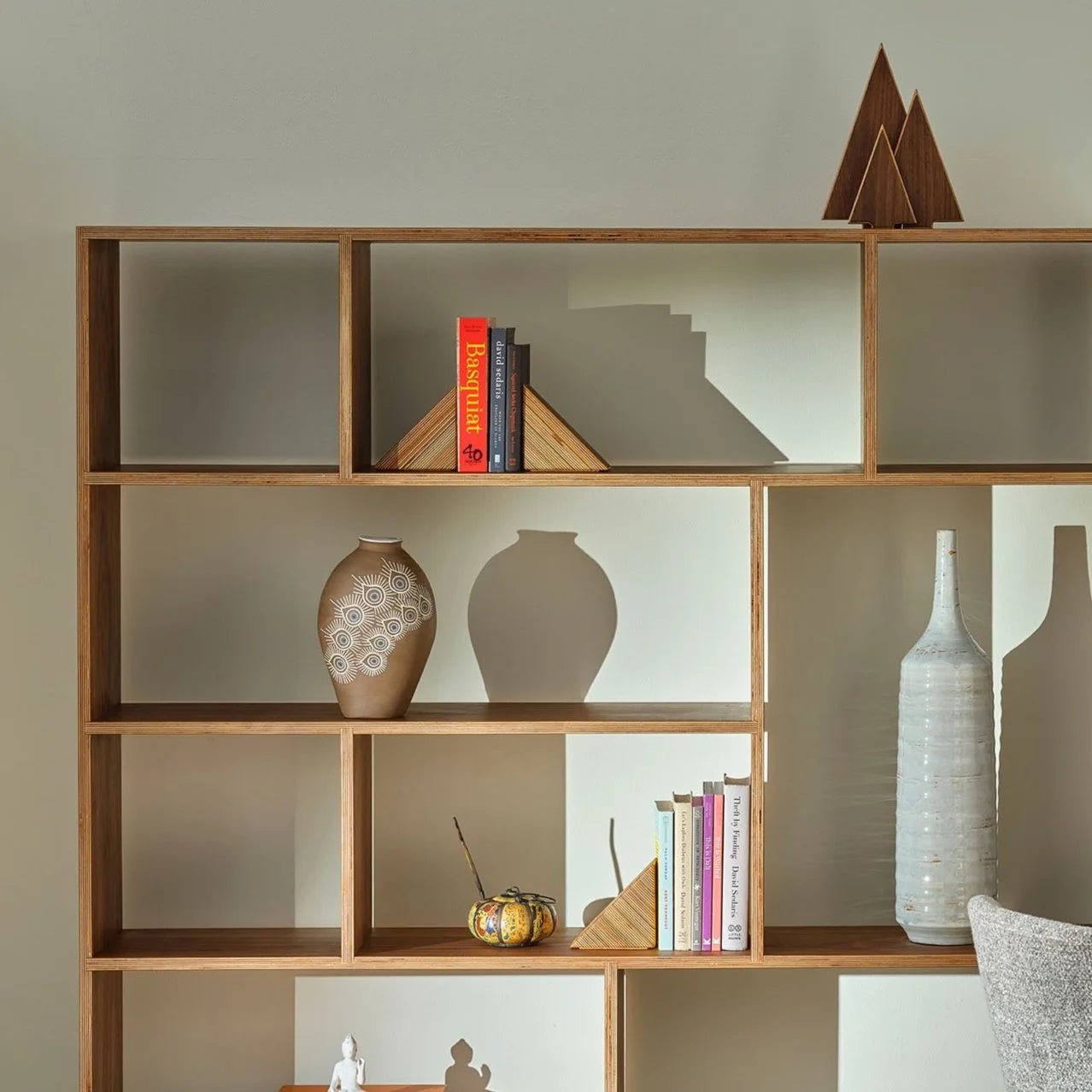 Styled walnut bookshelf with books, ceramic vases, and wooden tree sculptures on top