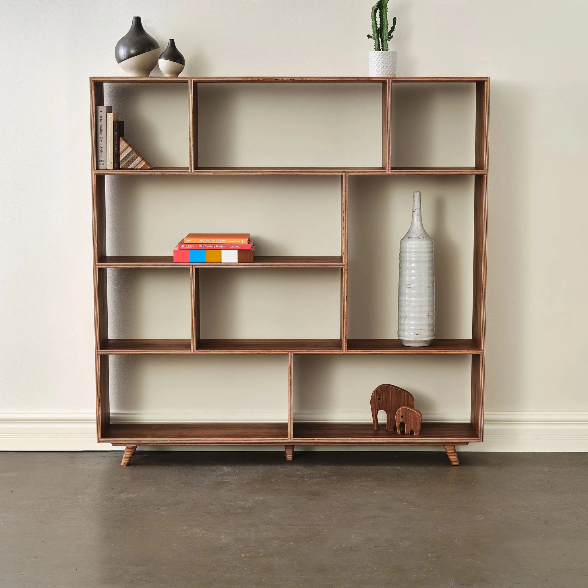 Staged wide walnut bookcase with ceramic vases, cactus, books, wooden elephant figures