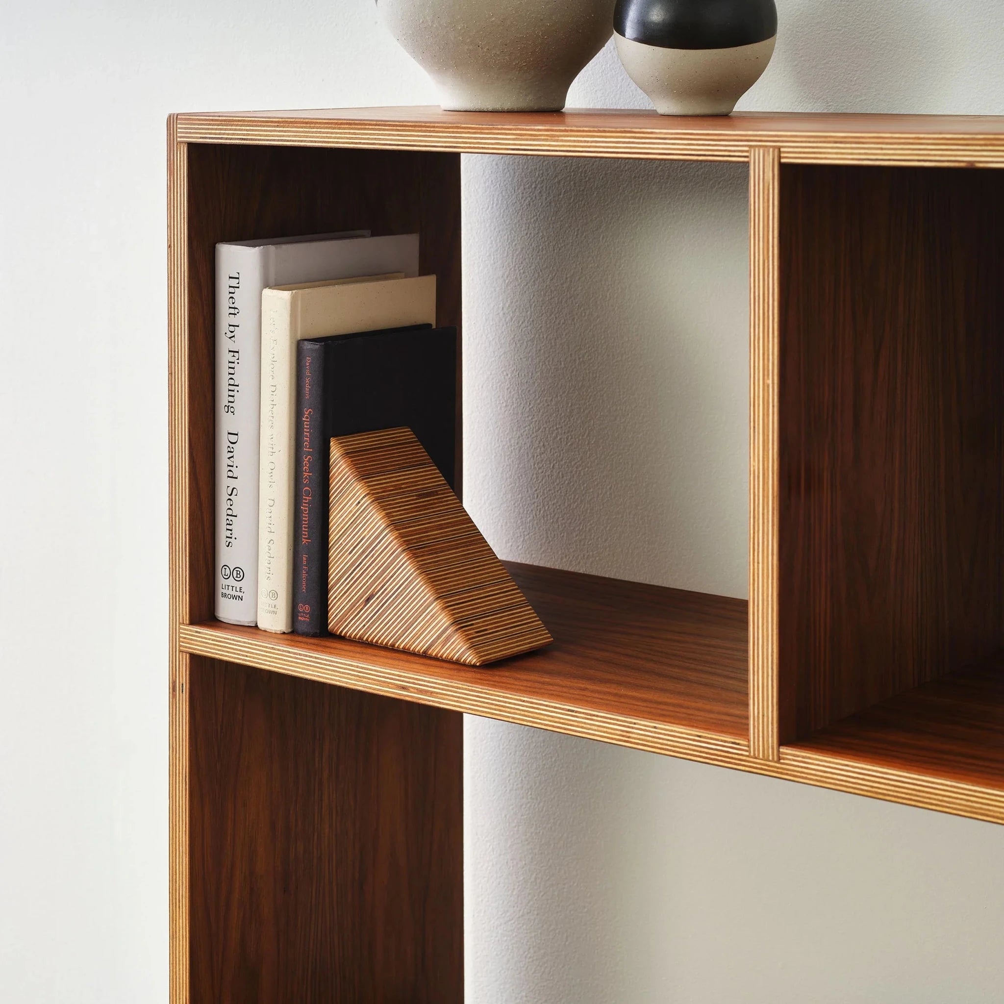Walnut bookcase closeup with books, plywood triangle bookend, ceramic vases on top shelf