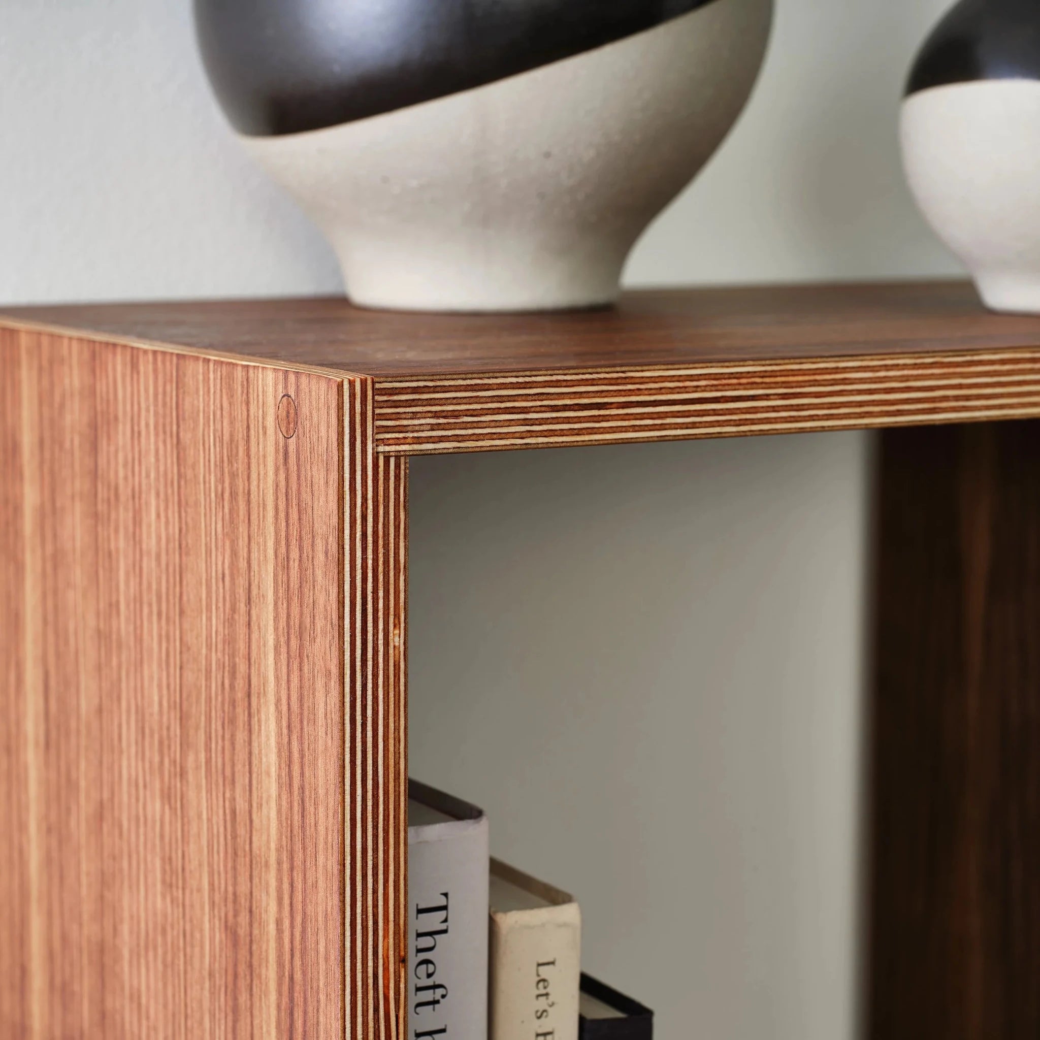 Close-up of walnut bookcase corner showing layered birch plywood edge and dotted vases
