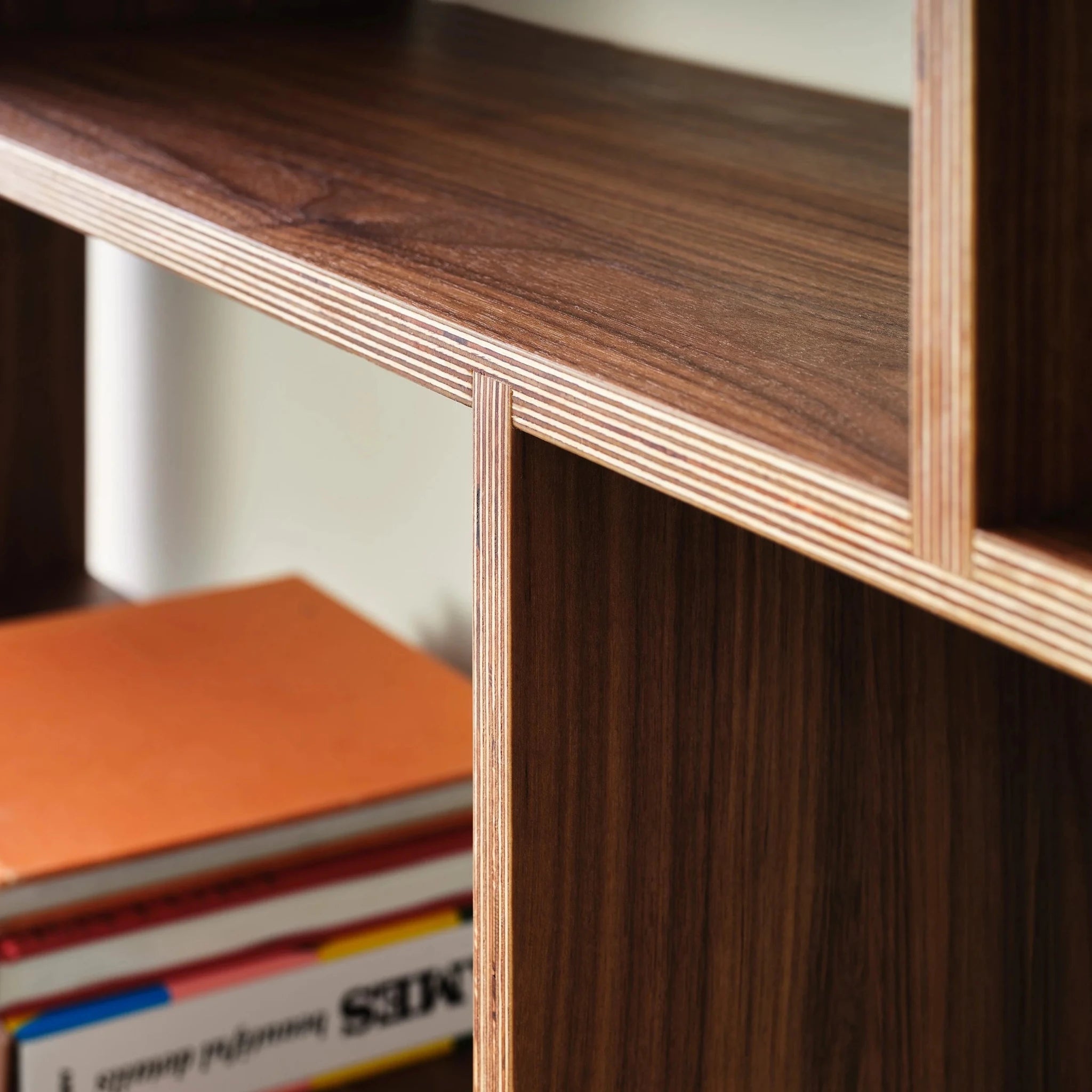 Detailed walnut bookcase joint with exposed layered birch plywood edge and books below