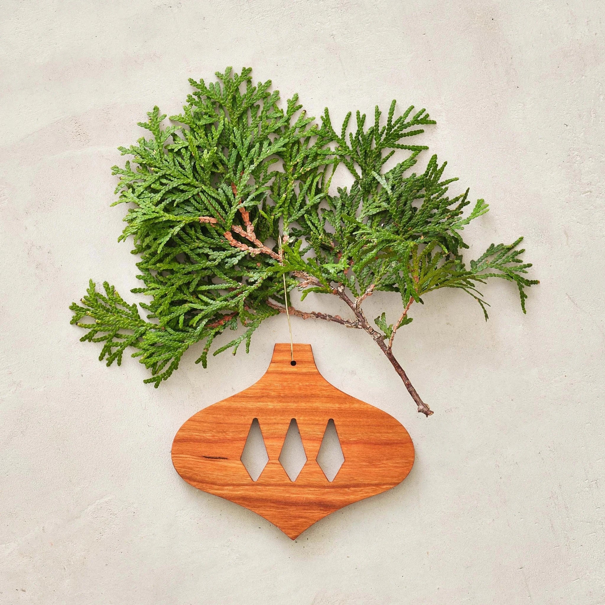 Cherry bulb ornament with diamond cutouts, styled beside green cedar sprig