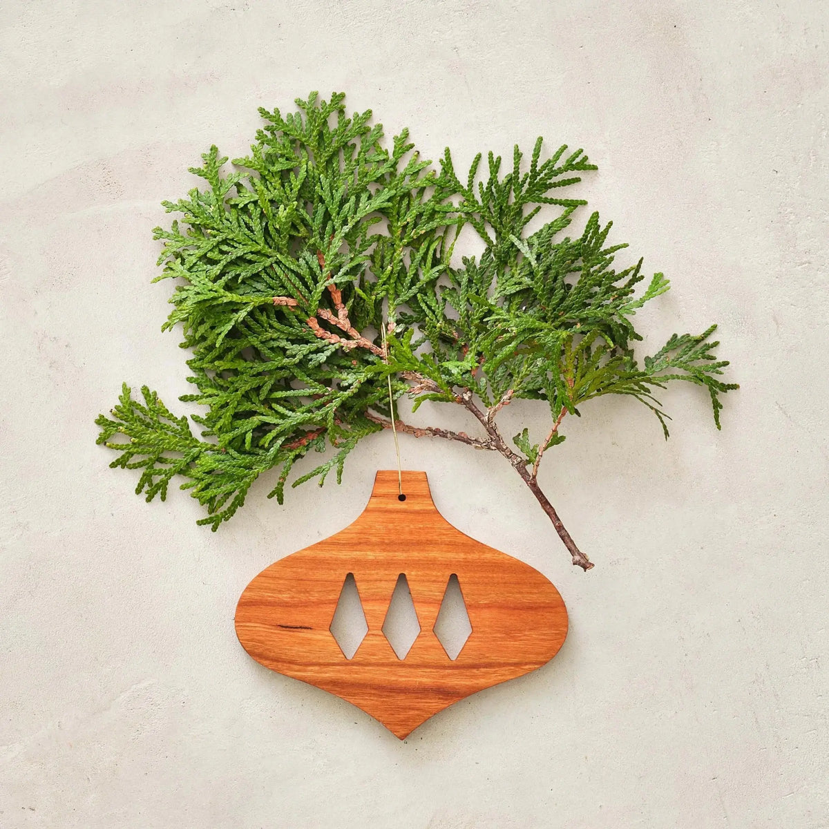 Cherry bulb ornament with diamond cutouts, styled beside green cedar sprig