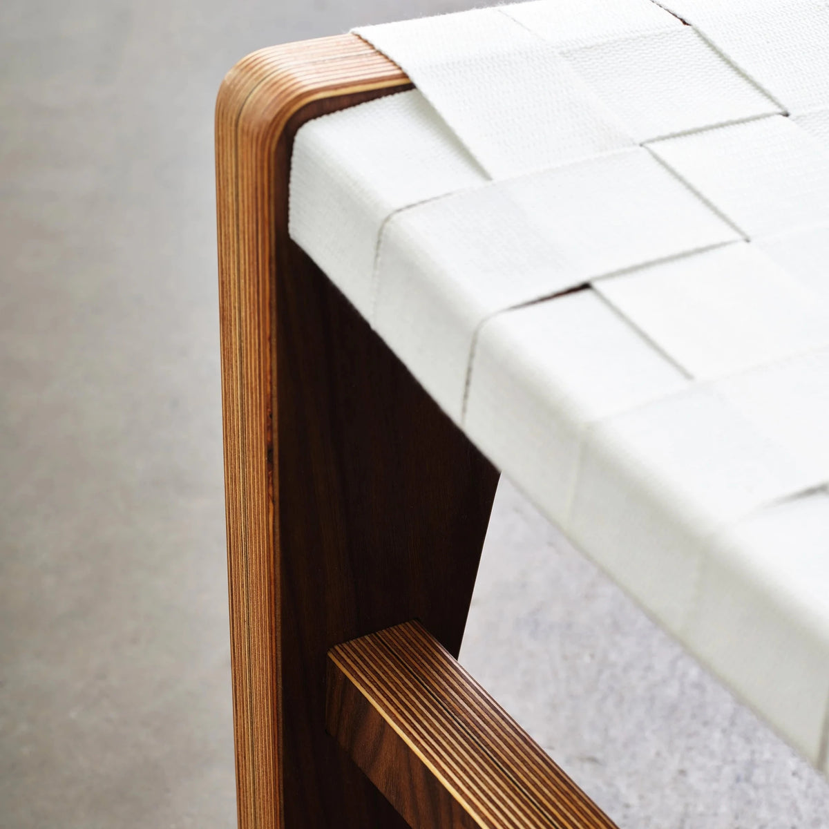 Rounded walnut ottoman leg showing layered birch plywood edge and white woven webbing