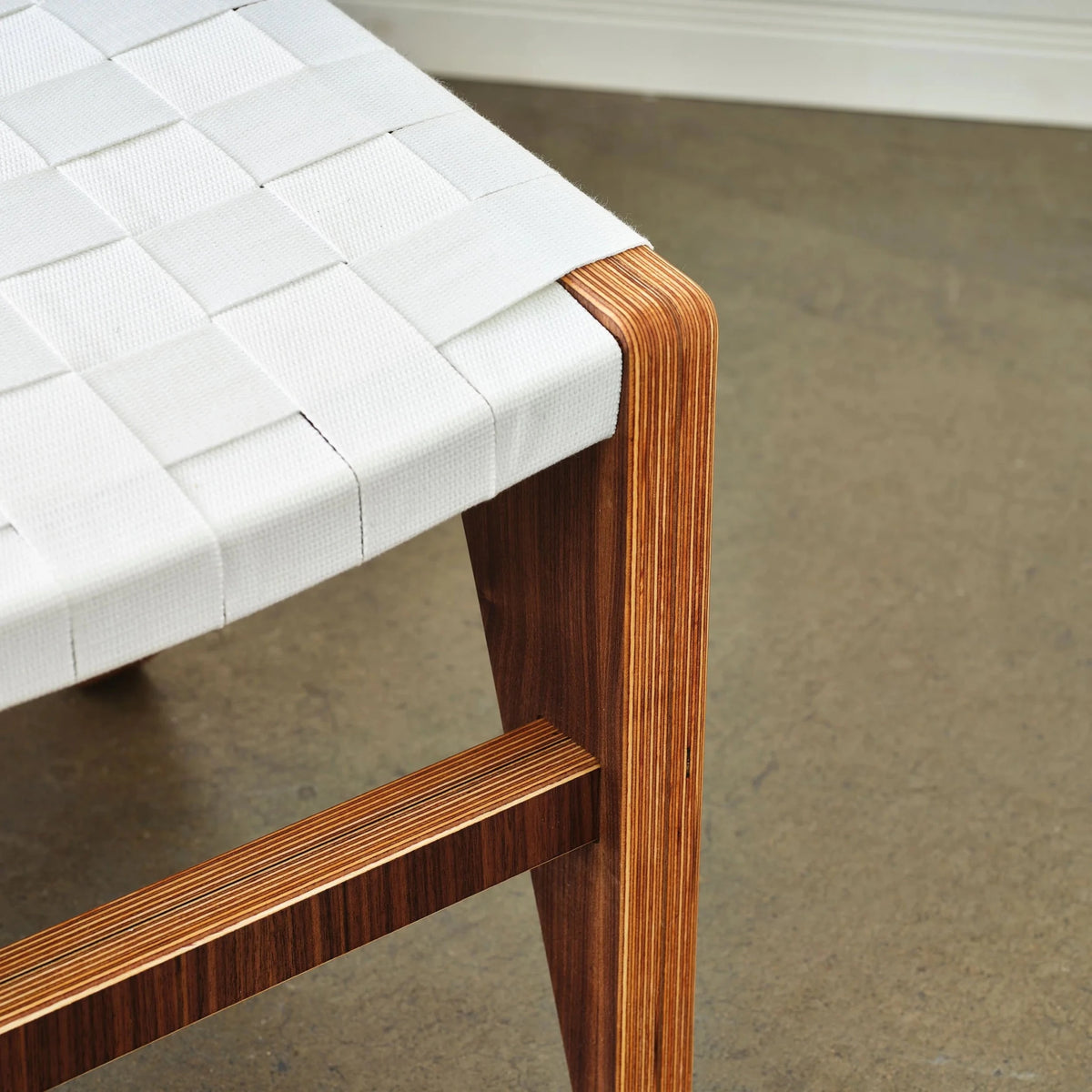 Ottoman corner detail: white woven straps, walnut frame with birch edge, concrete floor