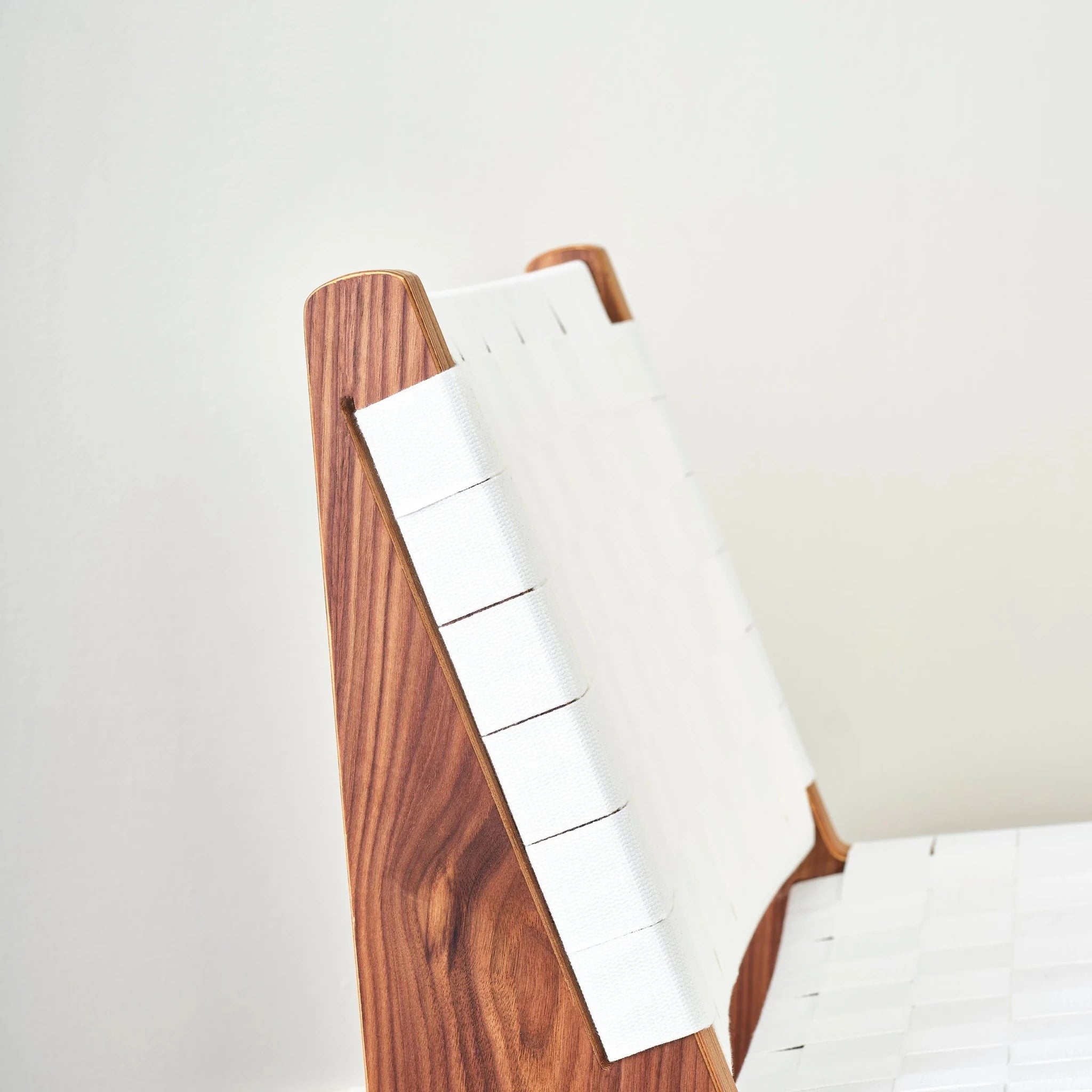 Side view of walnut chair back, white woven webbing straps wrapping around frame