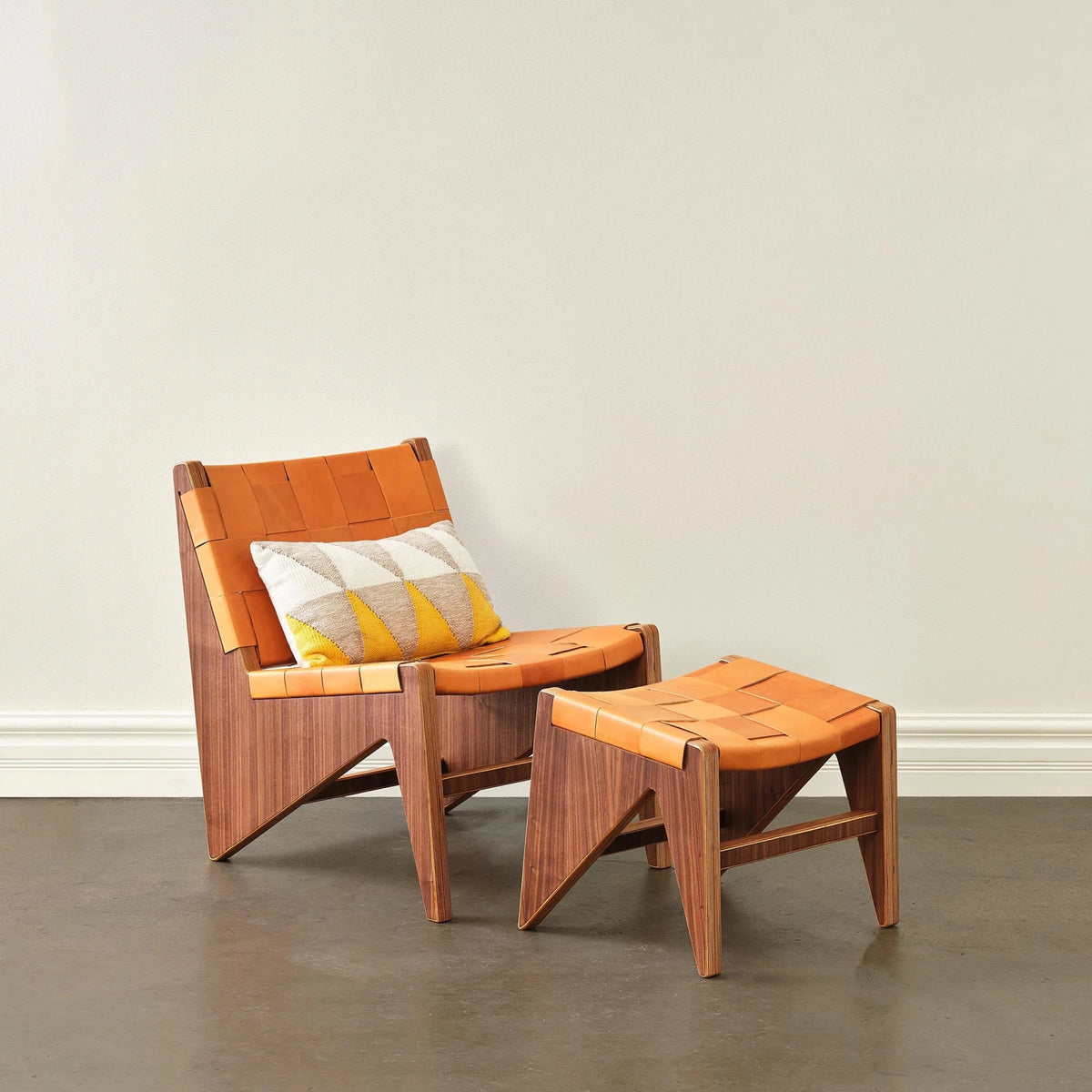 Walnut chair and ottoman, woven tan leather, geometric yellow lumbar pillow, staged white wall
