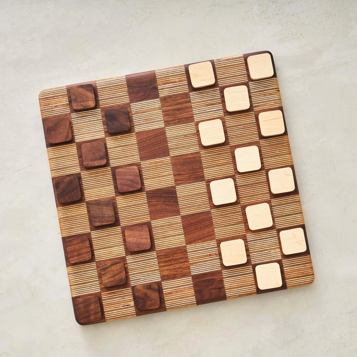 Overhead view of walnut and maple checkers discs set up on opposite board sides