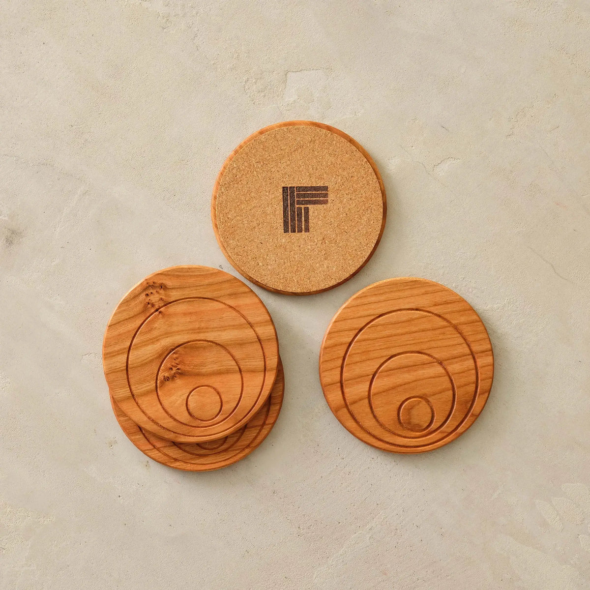 Cherry coaster set overhead, concentric-groove tops with one cork-backed logo coaster