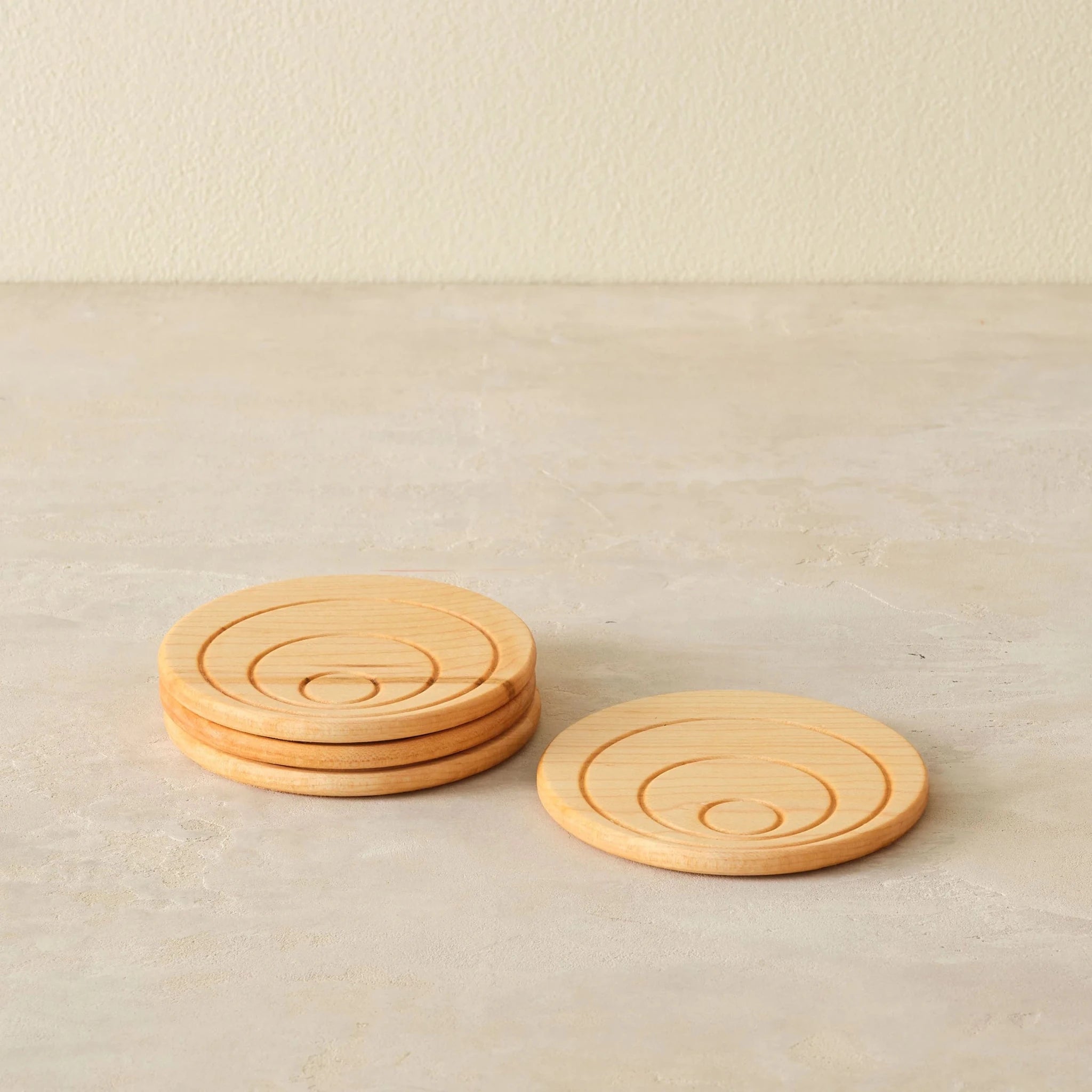Maple coaster set at front angle, single coaster propped beside stack