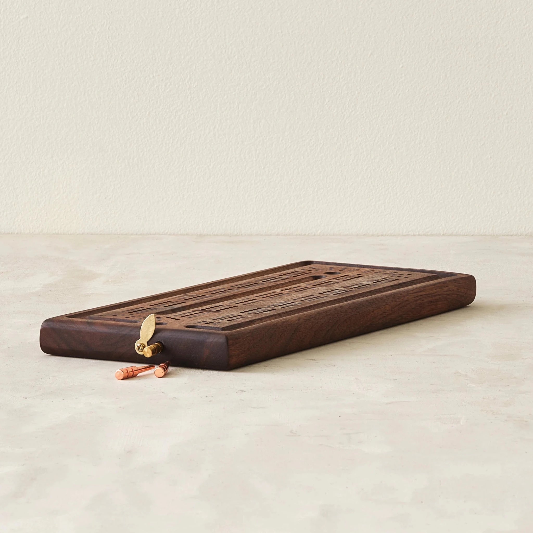 Walnut cribbage board angled, open brass latch, copper peg lying beside