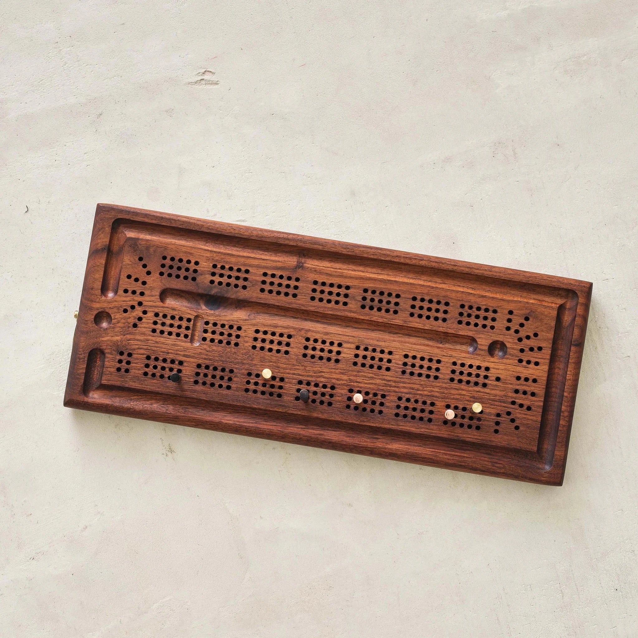Walnut cribbage board top view with brass and copper pegs on concrete