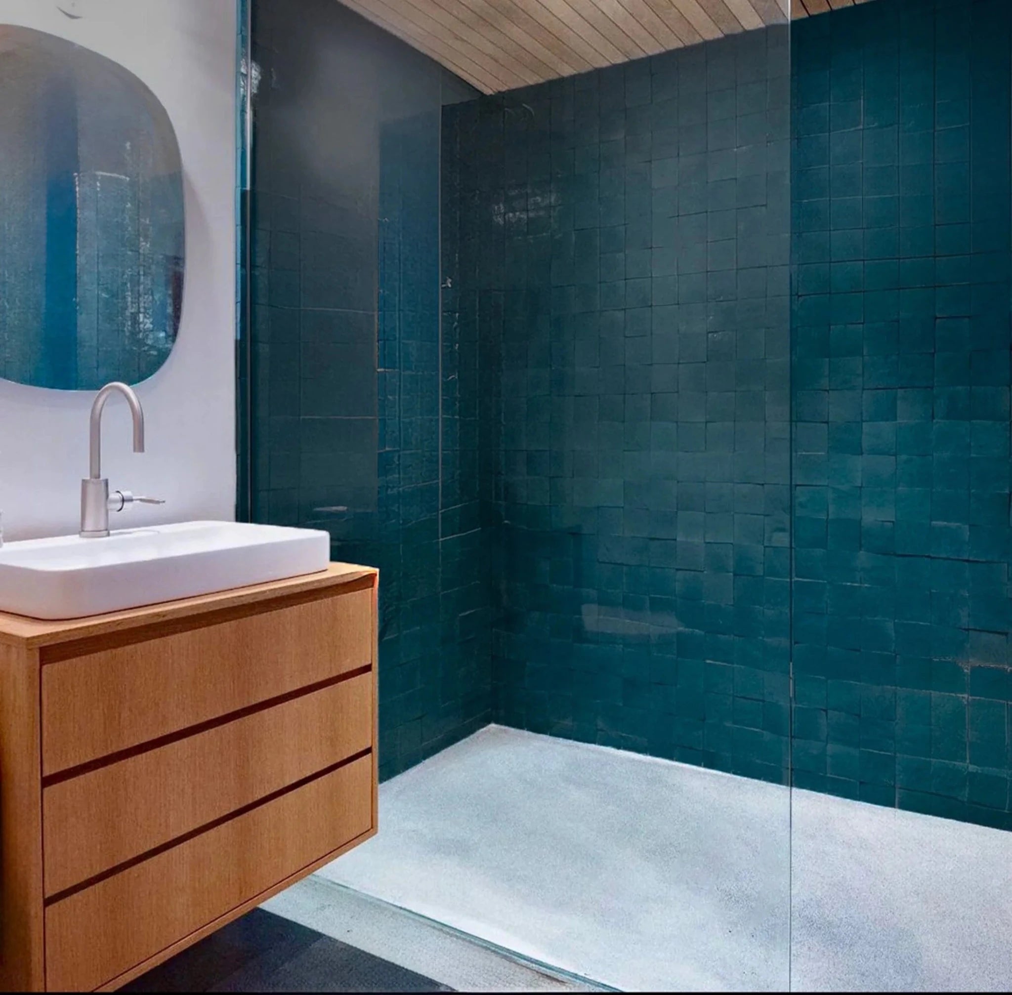 Floating oak vanity, white vessel sink, chrome faucet beside teal-tiled walk-in shower
