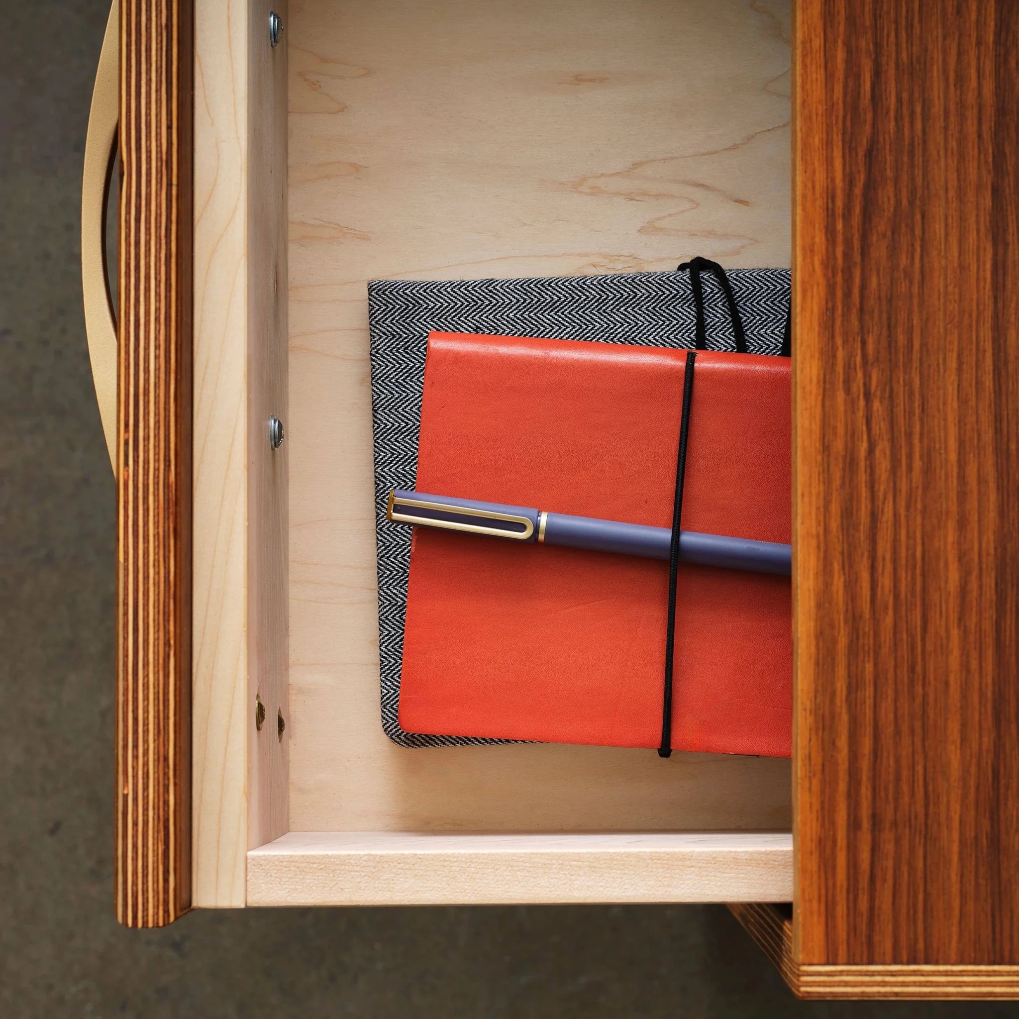 Overhead view of open desk drawer, orange leather journal and pen inside