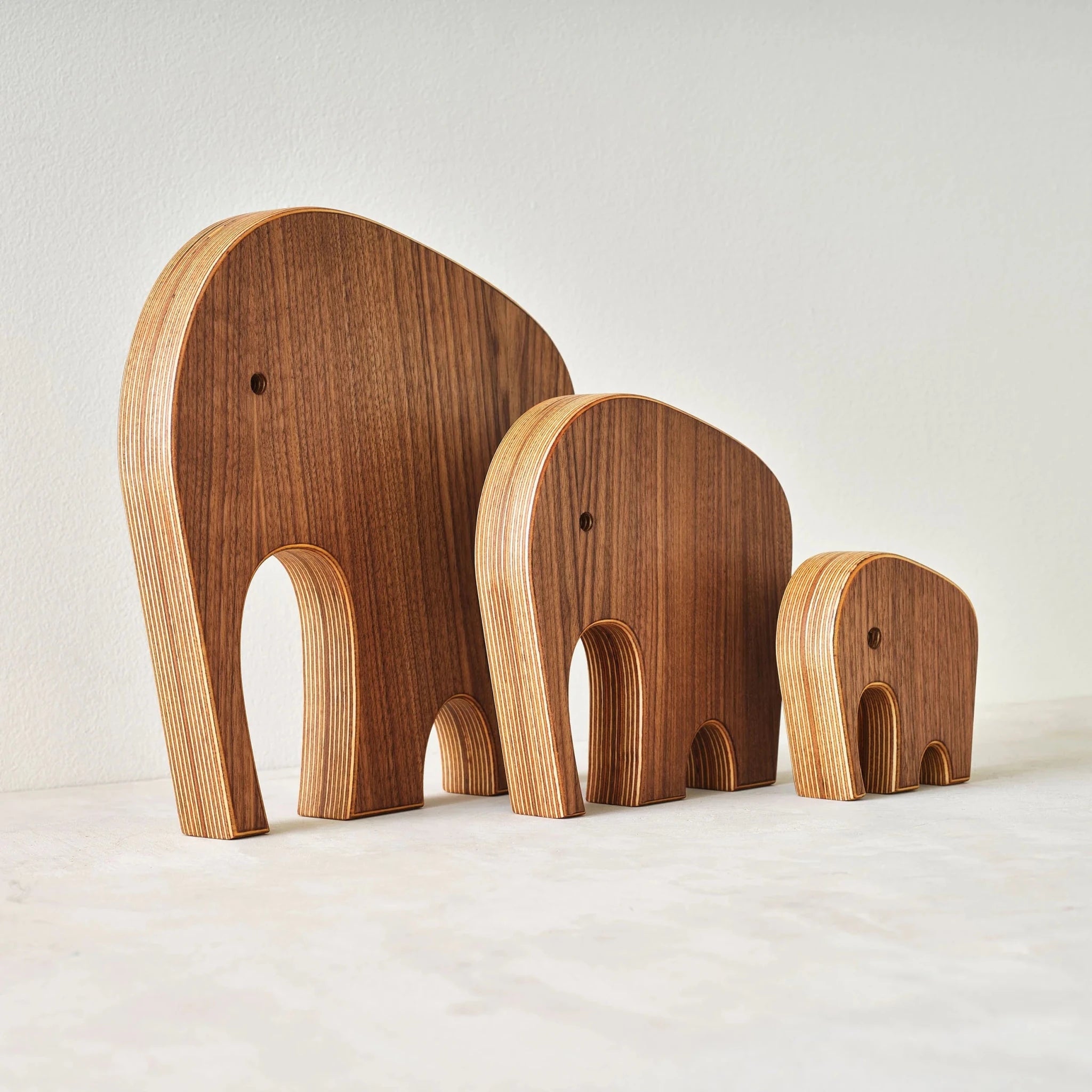 Three graduated walnut elephant sculptures, angled view revealing layered Baltic birch plywood edges