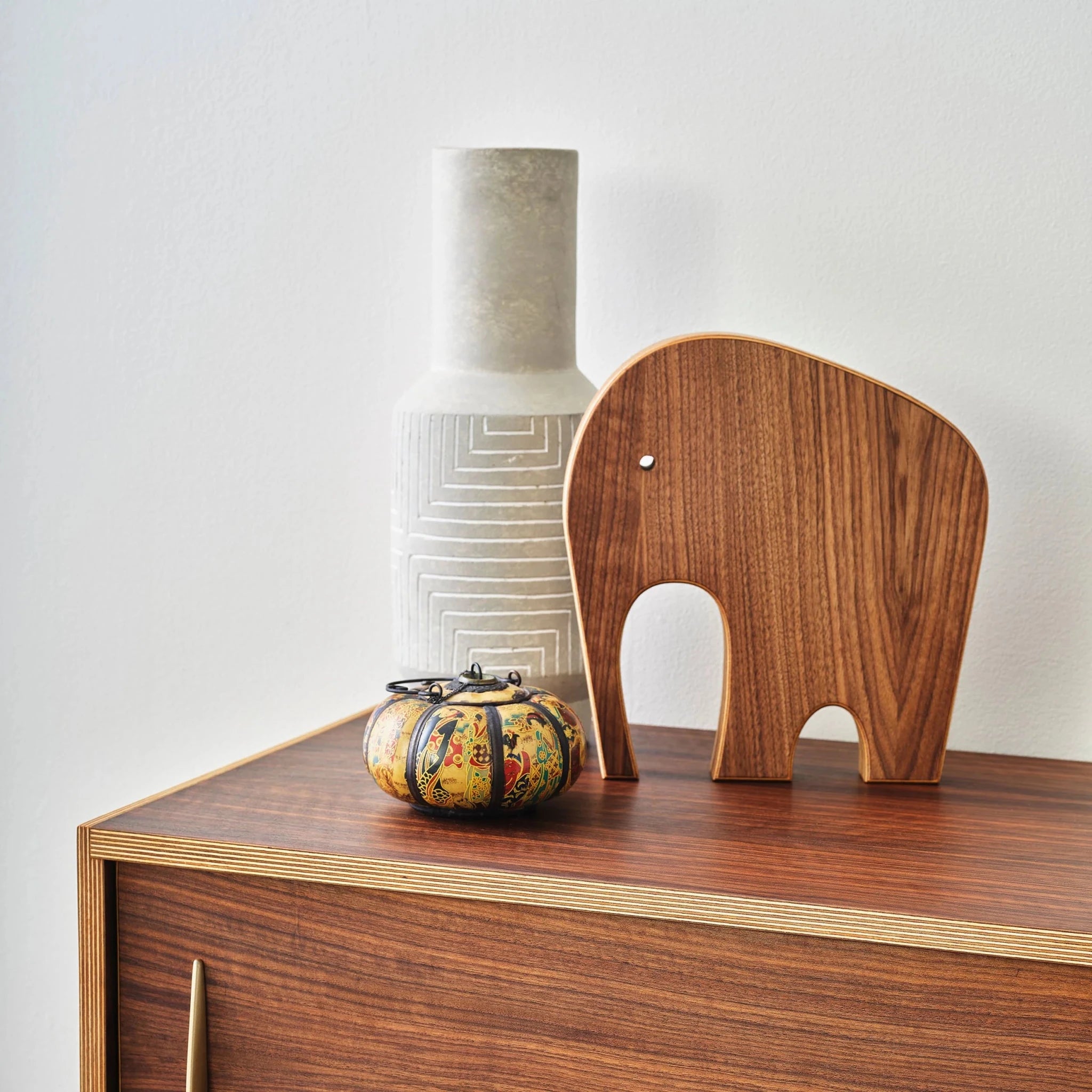 Walnut elephant sculpture on sideboard beside gray patterned vase and painted decorative jar
