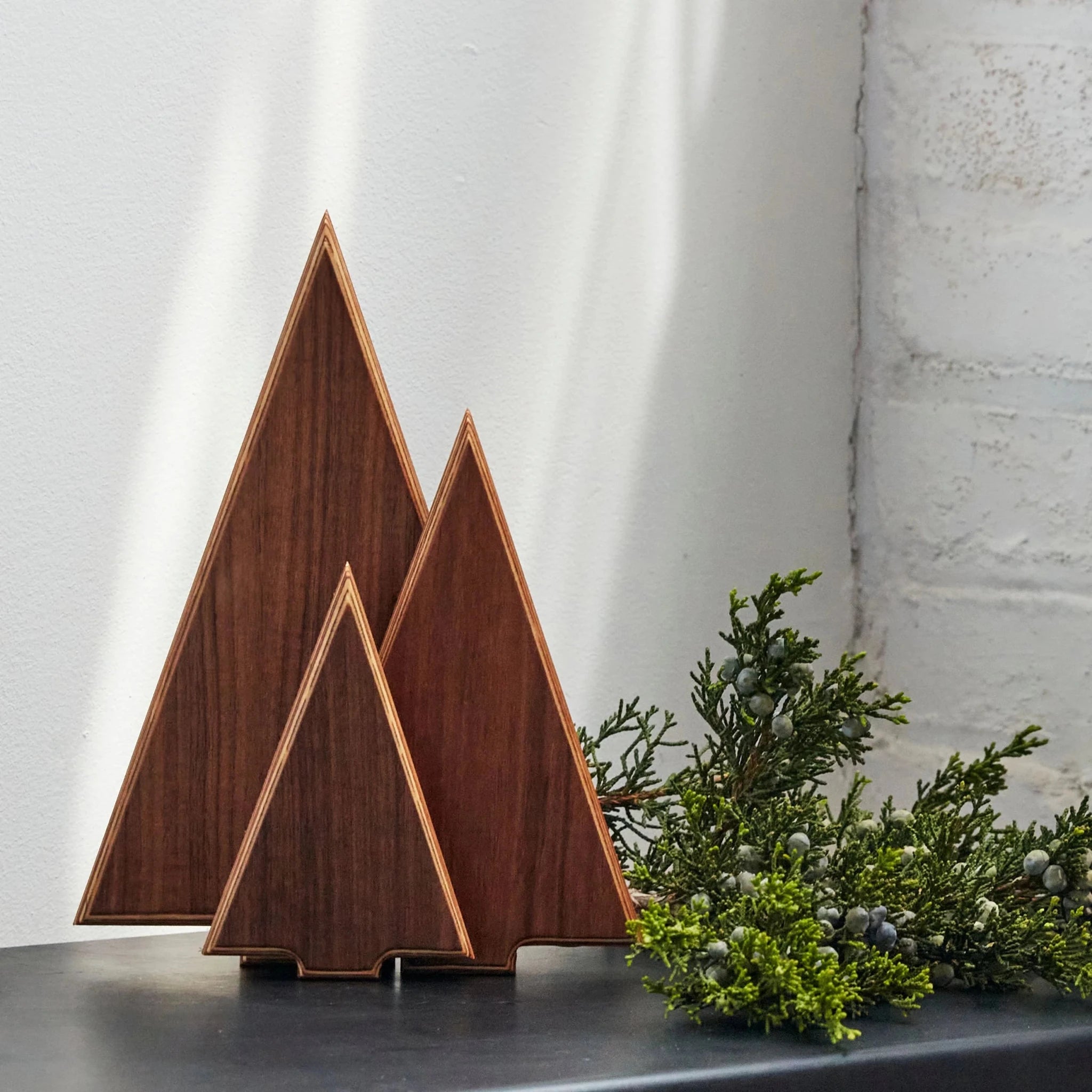 Walnut tree sculptures styled with juniper greenery on black mantel