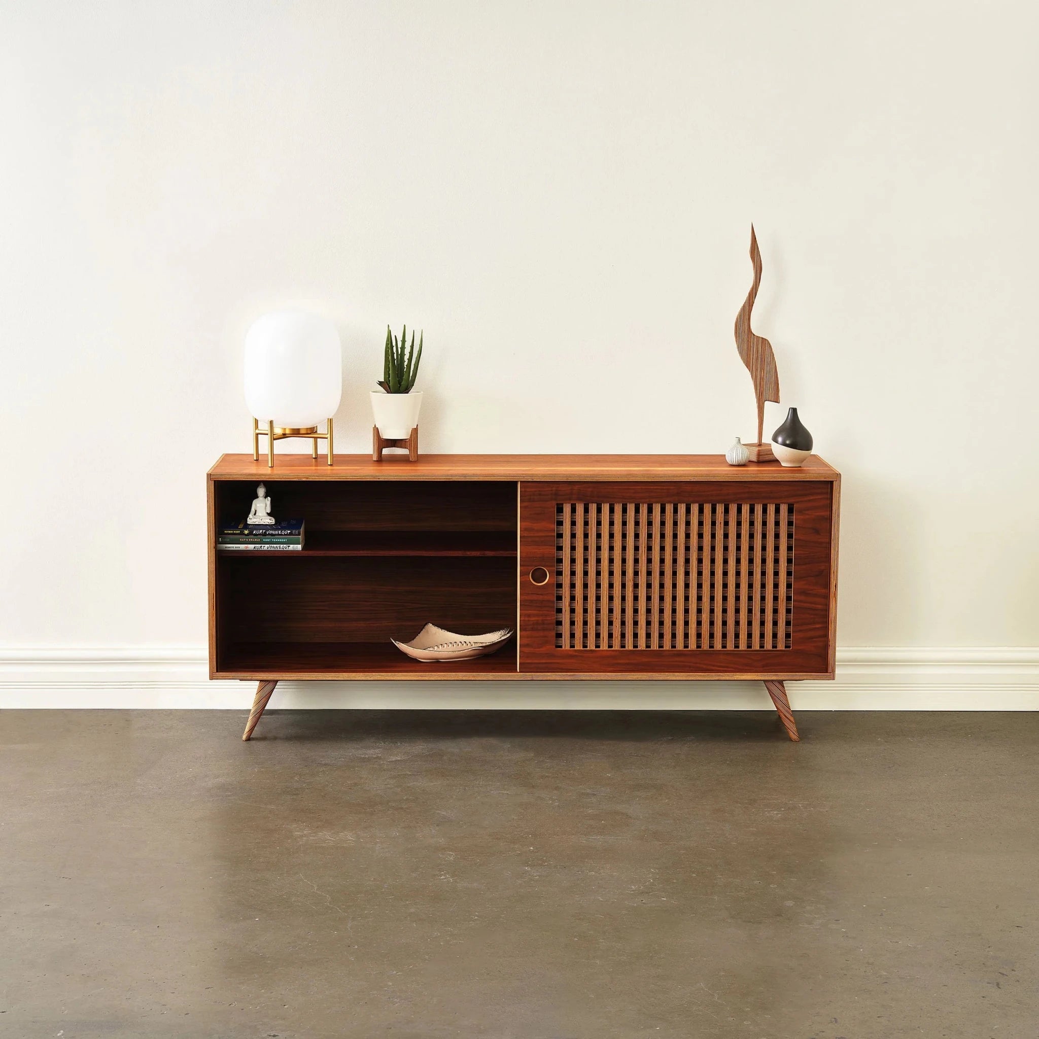 Media console with slatted door slid right, open left shelf holding books, decor styled