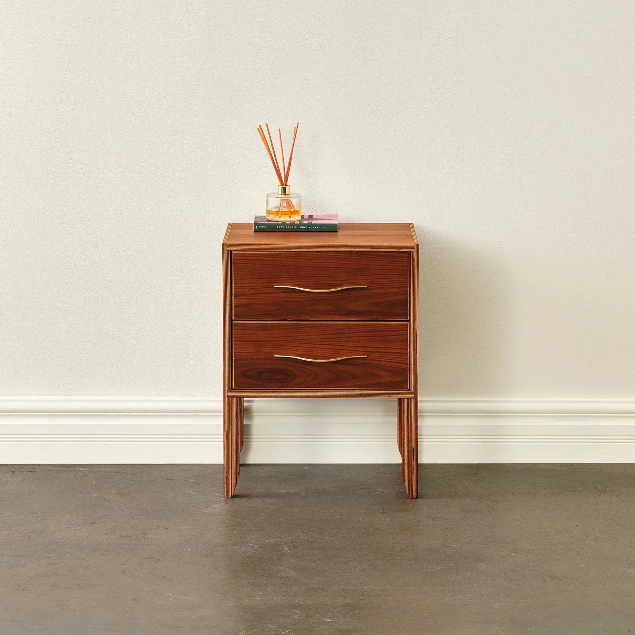 Front view of walnut nightstand, closed drawers, brass pulls, diffuser and book styled on top