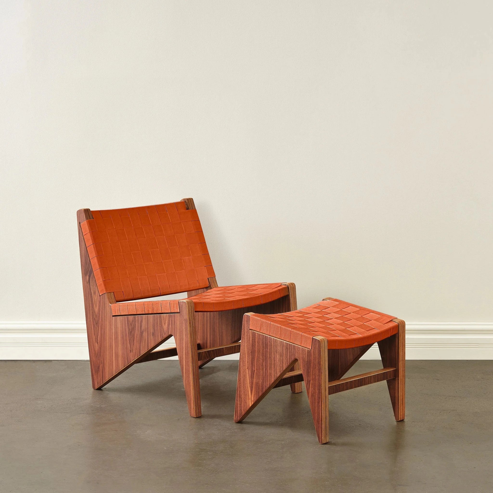 Walnut accent chair and ottoman with woven rust-orange fabric straps, front view, concrete floor