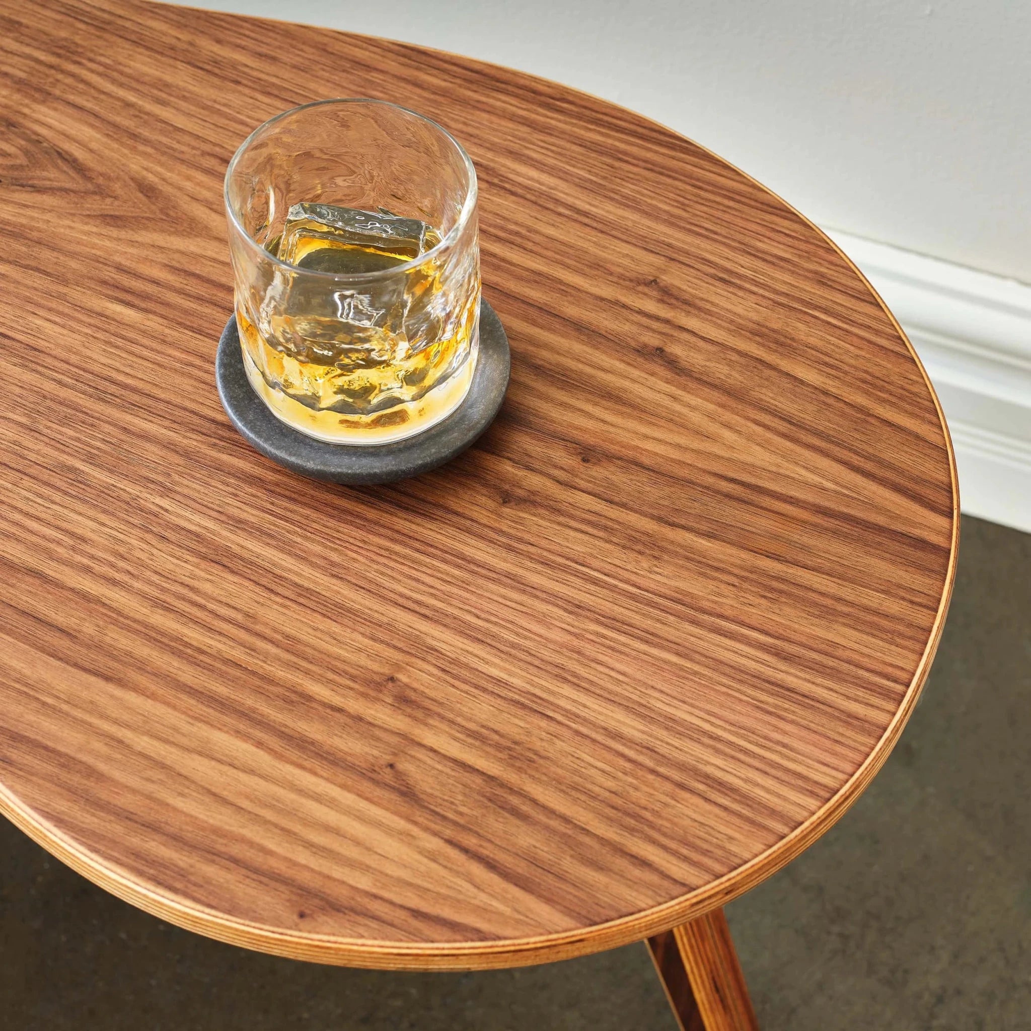 Overhead view of walnut cocktail tabletop with whiskey glass on stone coaster, plywood edge