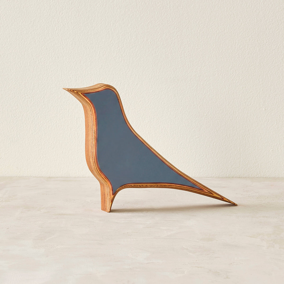 A modern bird-shaped decorative sculpture made of layered wood with a matte slate-blue laminate in a neutral space.