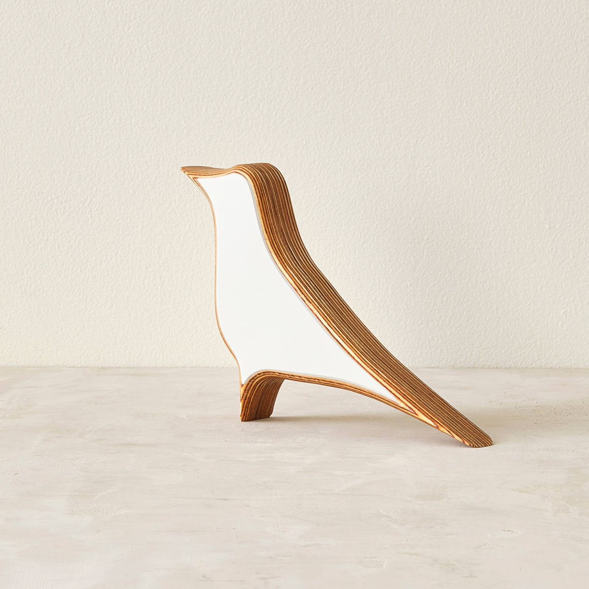 A modern bird-shaped decorative sculpture made of layered wood with a matte white laminate in a neutral space.
