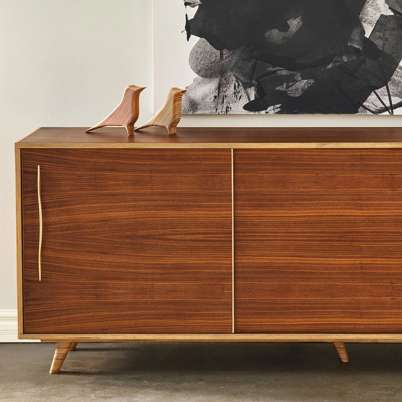 Two Robin bird sculptures atop walnut sliding-door sideboard, styled beside black-and-white artwork