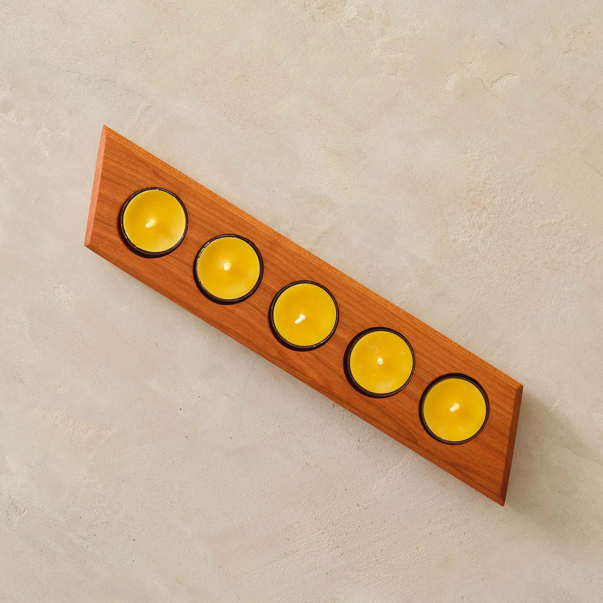Top-down cherry tealight bar holder holding five yellow candles on stone surface
