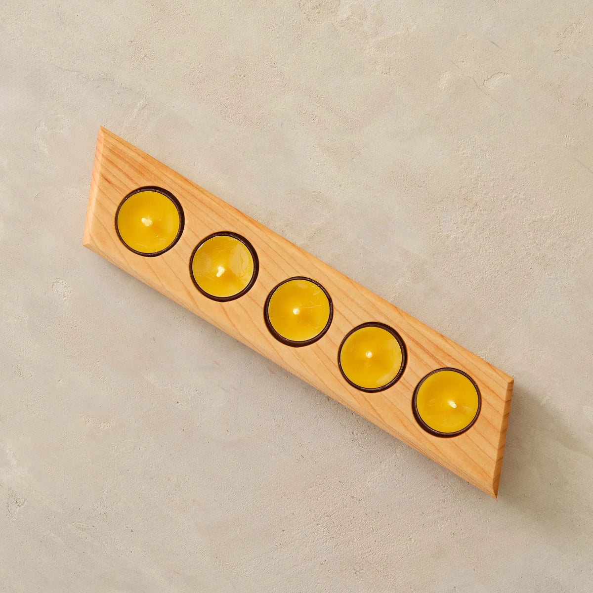 Overhead maple tealight bar holder with five yellow beeswax candles, stone background