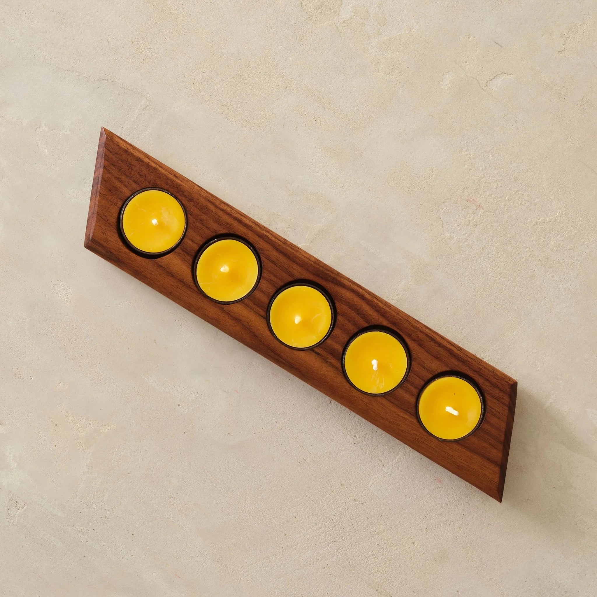 Overhead walnut tealight bar holder, five yellow beeswax candles, stone background