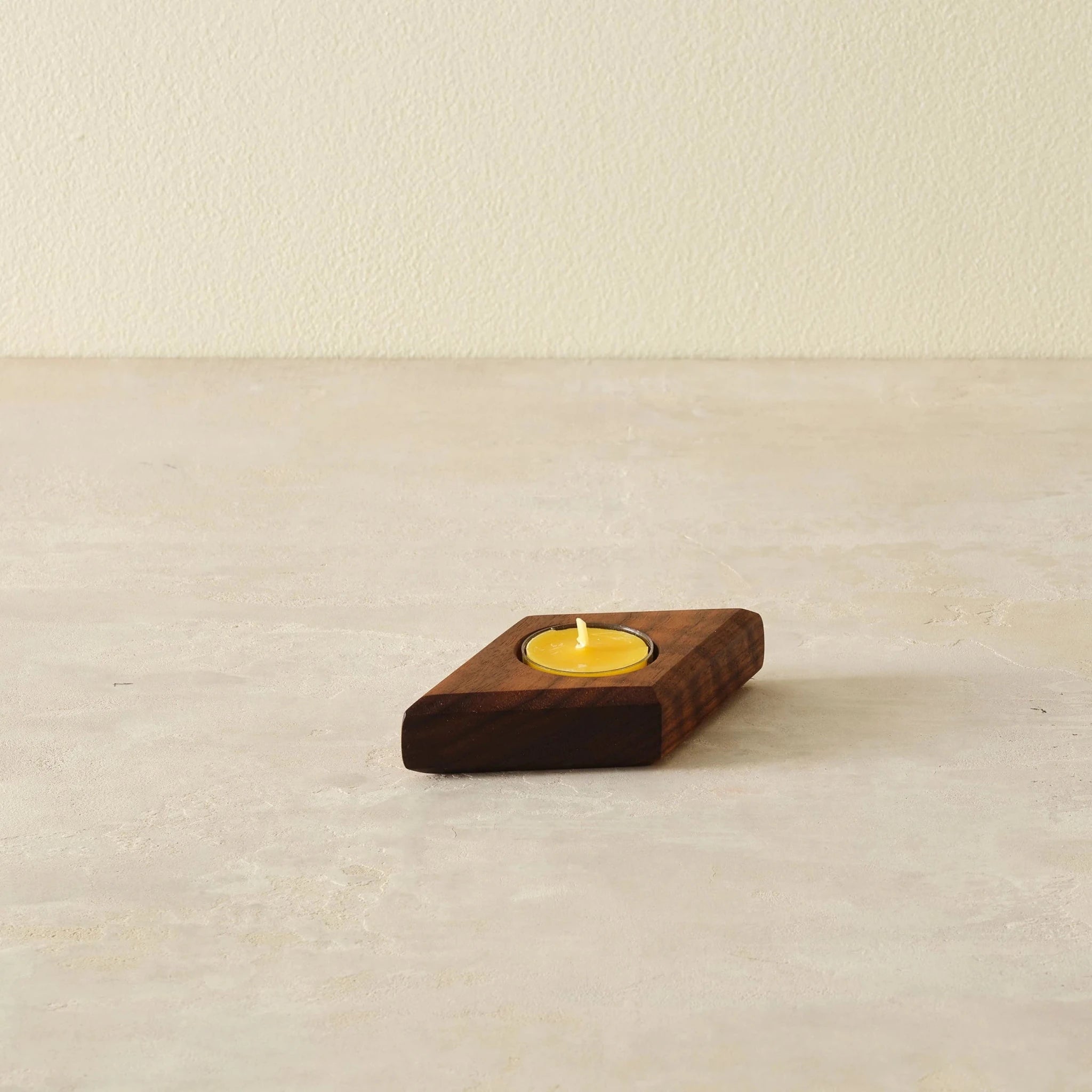 Single walnut tealight holder with one yellow beeswax candle on stone surface