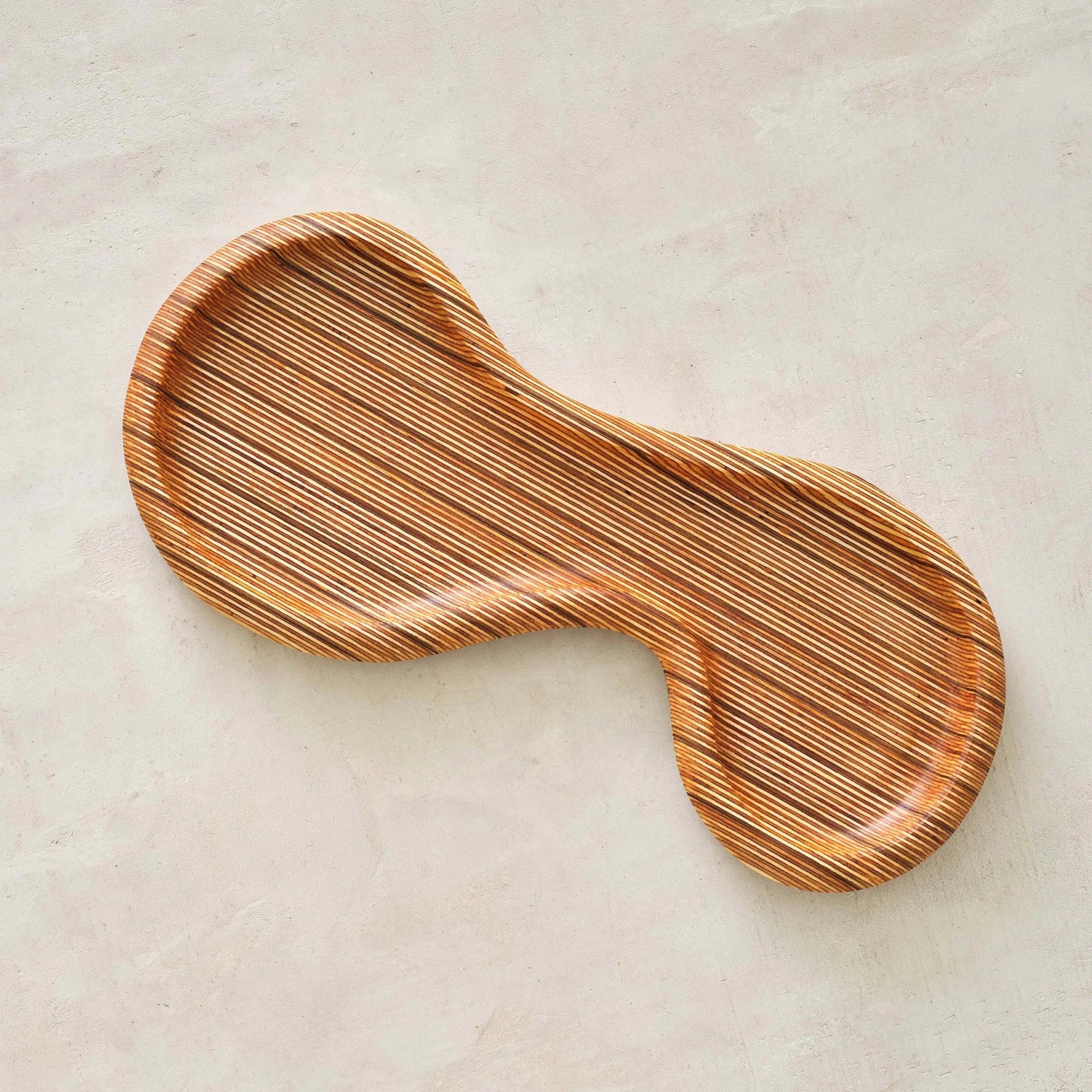 Curved peanut-shaped wooden tray top view, striped layered birch grain, plaster surface