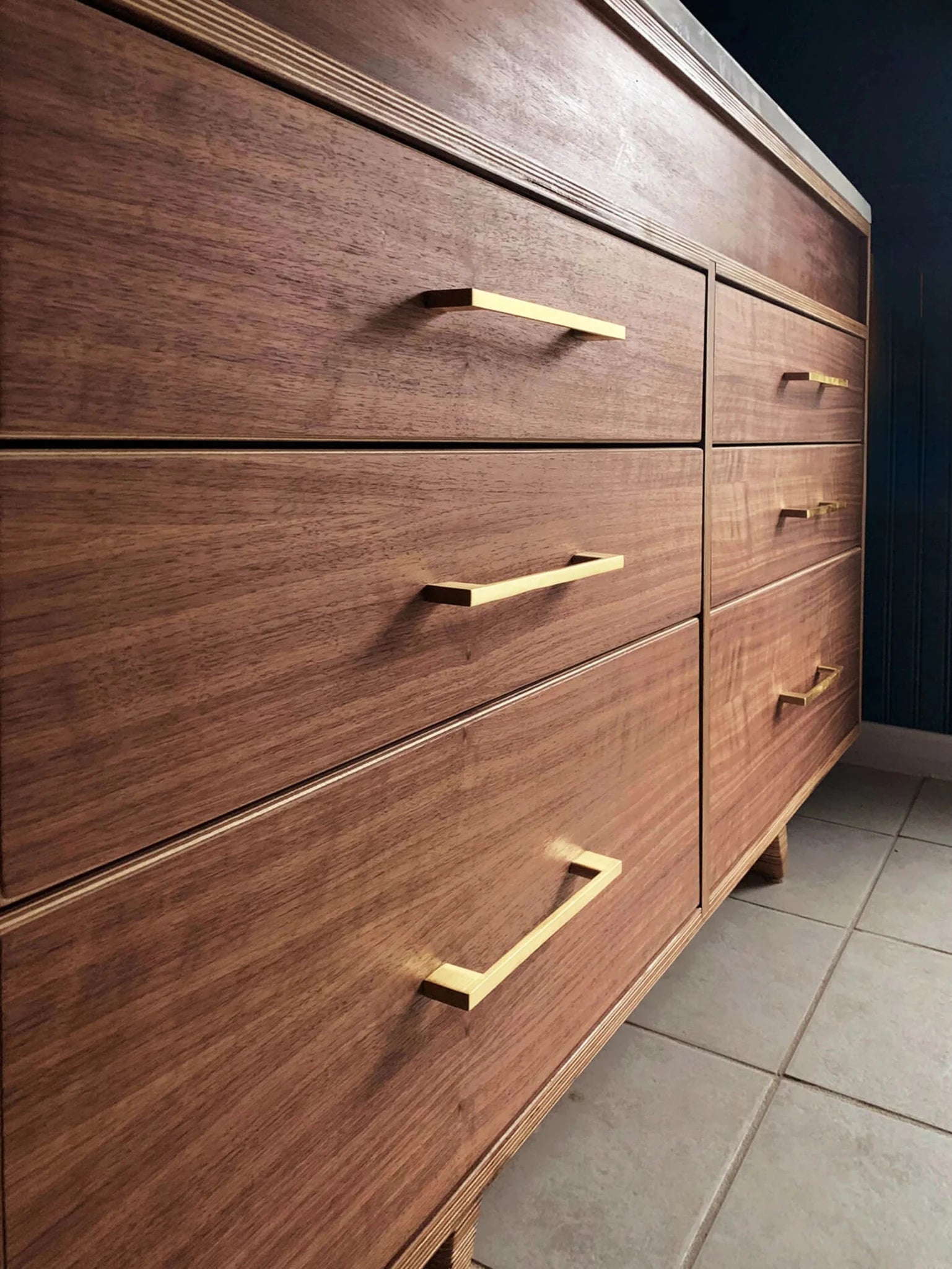 Close-up angled walnut vanity drawers with brass bar pulls, plywood edge, wood grain
