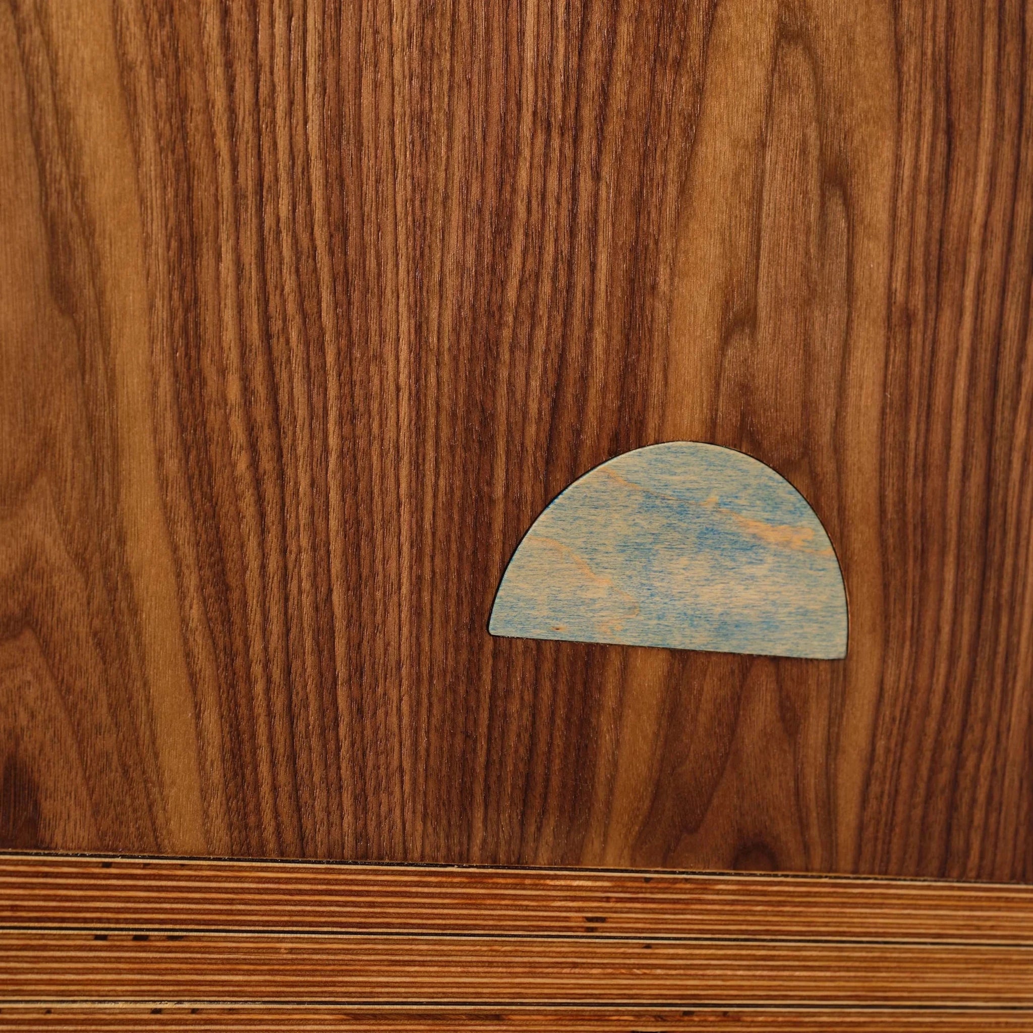 Closeup of Earthrise walnut art with blue half-moon sun inlay near birch base