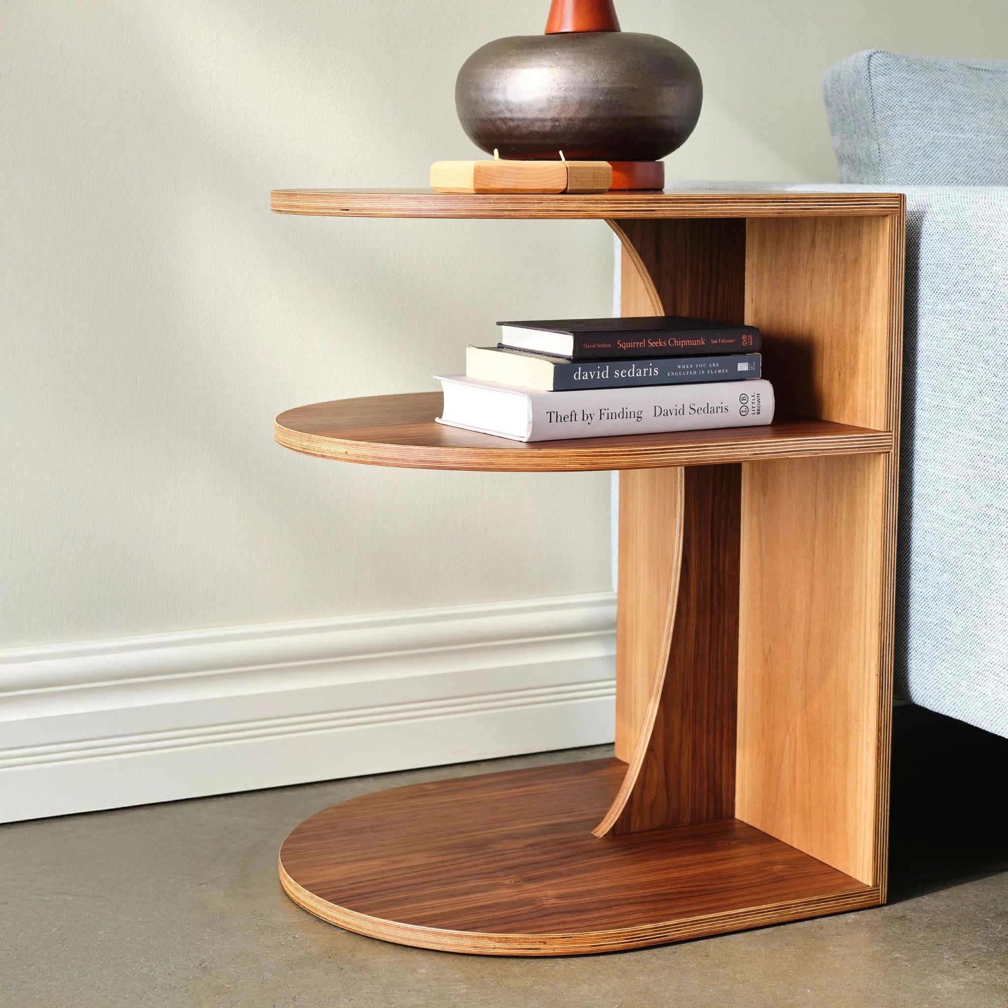 End Table No. 2, walnut two-tier C-shape, books stacked, vase, by sofa